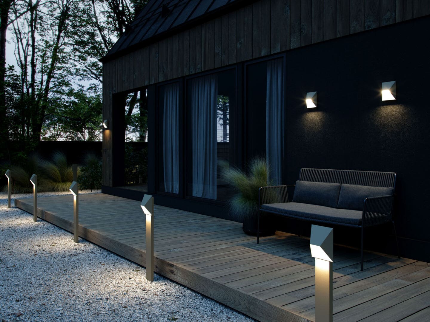 A modern black timber home with floor to ceiling windows. Exterior lighting illuminates the house after dusk