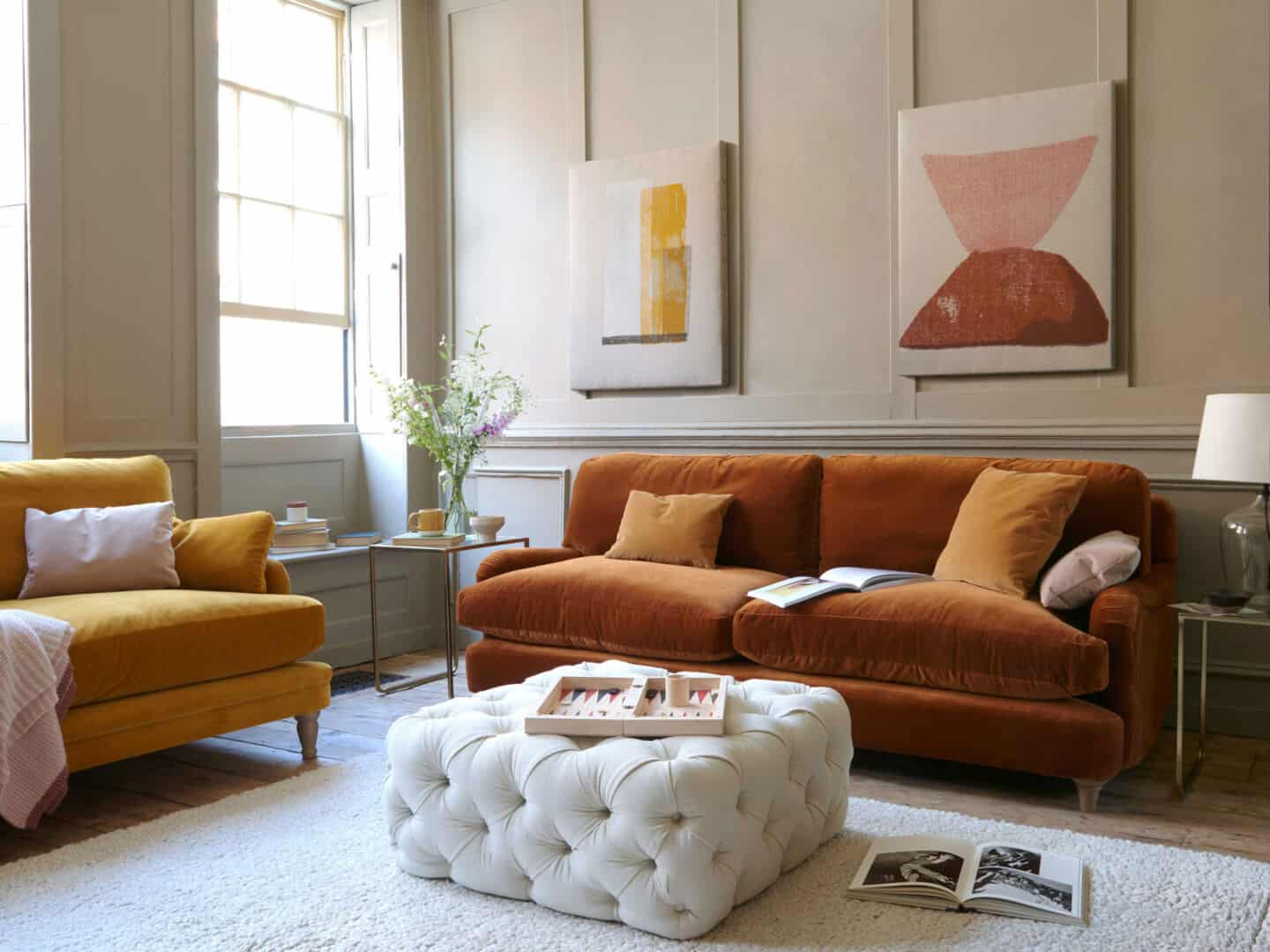 Autumnal Hues in interiors -Loaf Jonesy Sofa in Praline with abstract artwork on the wall behind and a white cushioned pouffe in front