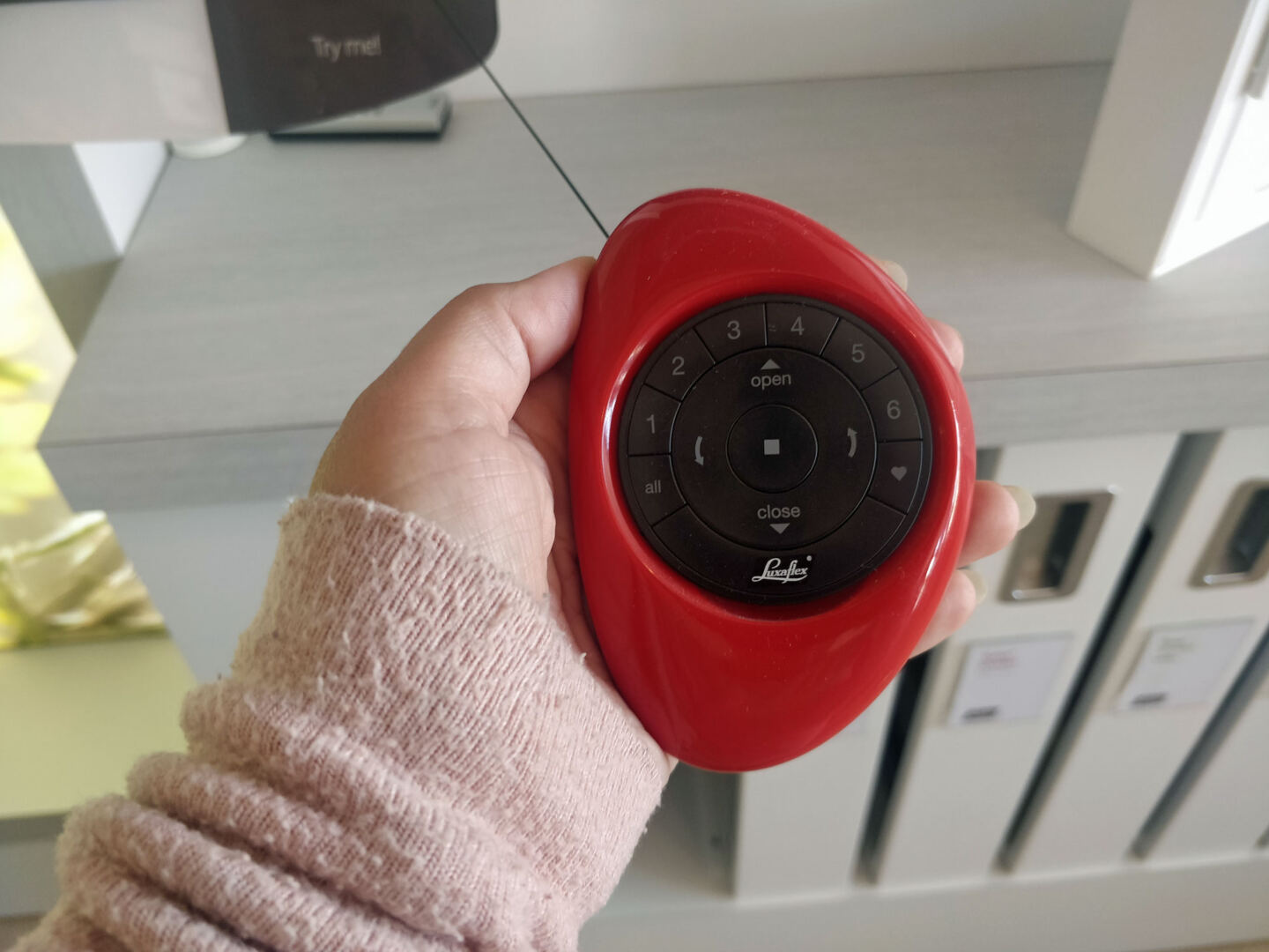 A hand holding a red Luxaflex blinds Pebble remote control