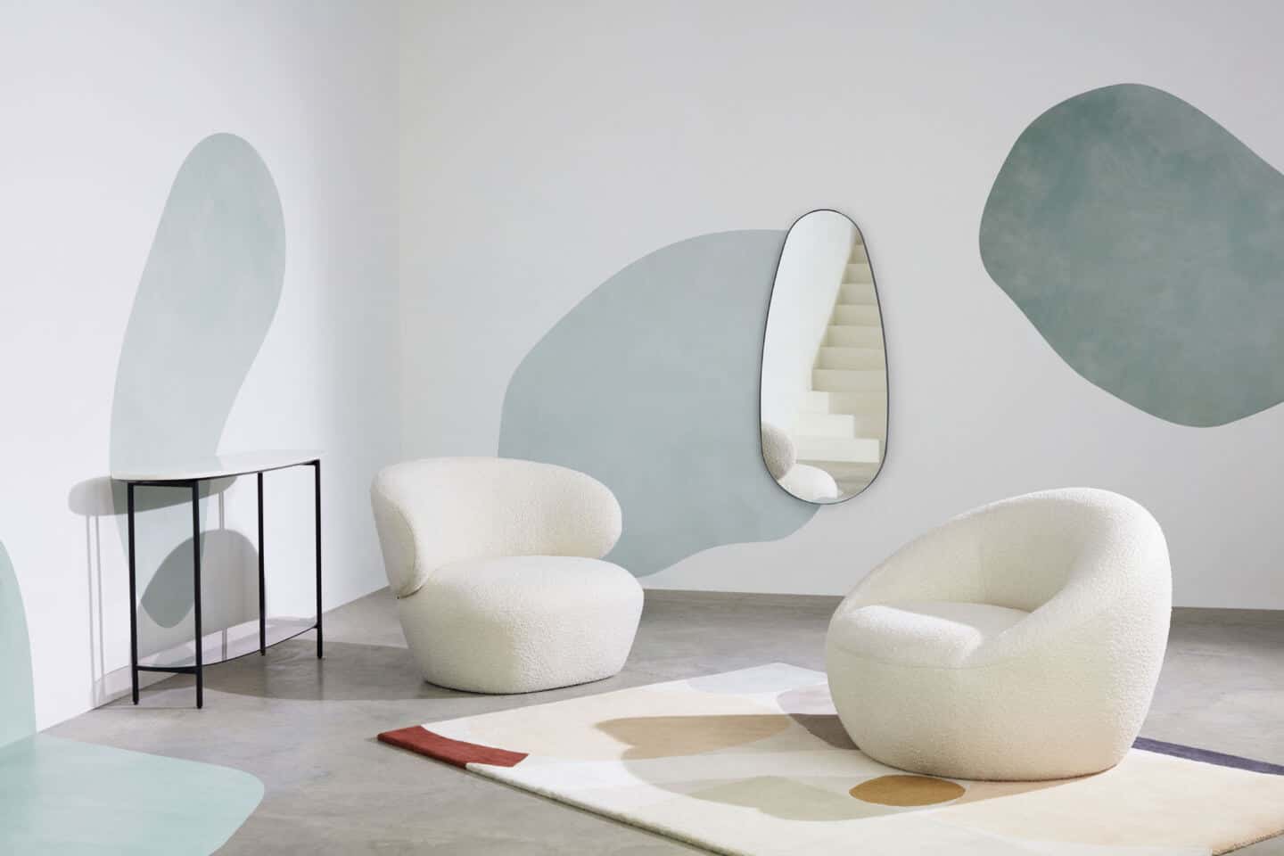 Room set by Made.com featuring two curved chairs on a rug with a console table and mirror behind. A great way of including organic shapes in interiors is to paint them on the walls.