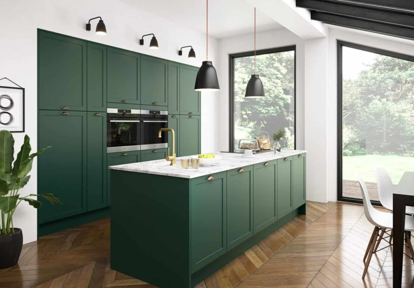 Magnet's Dunham Kitchen in Forest Walk. A deep dark green kitchen island with marble effect worktop in front of a run of green wall cabinets. Two large windows allow light to flood the kitchen