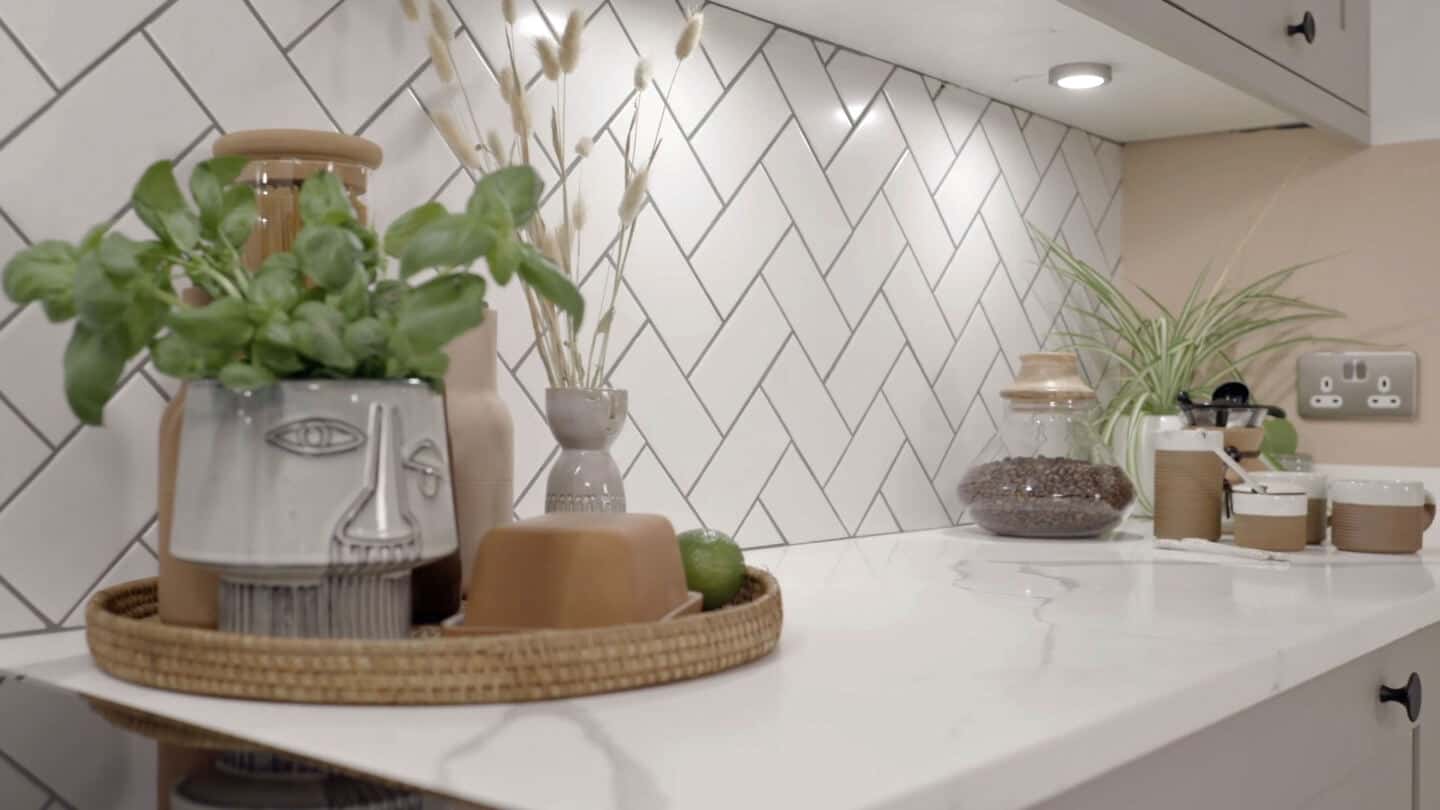 Biophilic kitchen designs provide a multi-sensory experience through natural materials and textures. Here kitchen accessories are displayed on a marble effect worktop.