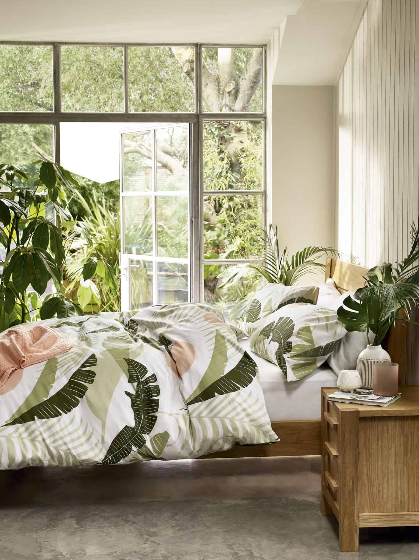 Nature in interiors. SS20 trend Botanical by M&S. Sonoma bedding on a wooden double bed in front of french doors with a garden outside