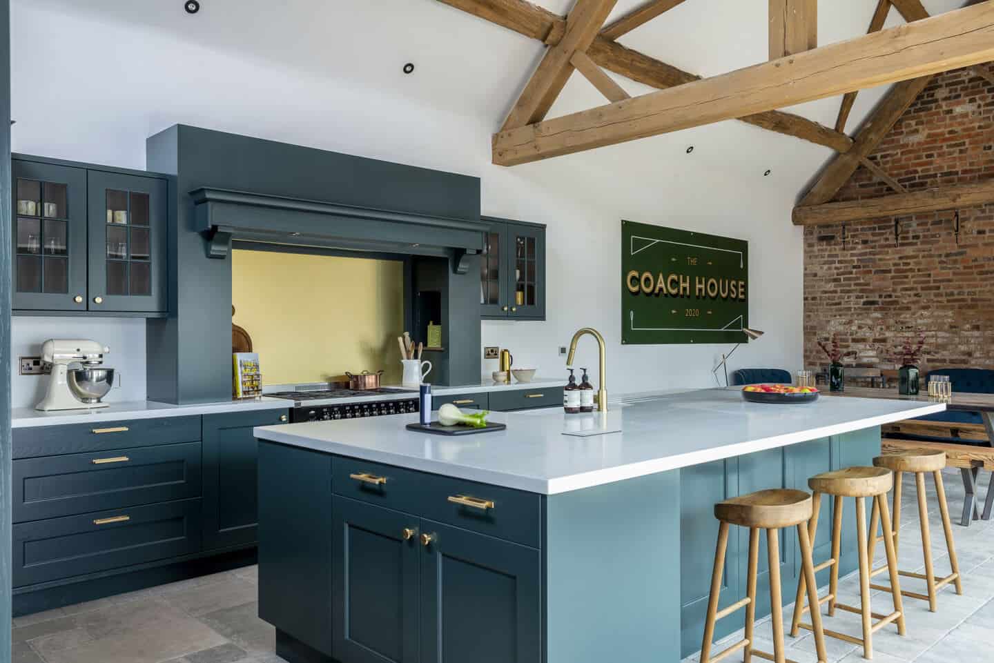 A navy blue kitchen with kitchen island, vaulted ceiling and exposed brick wall