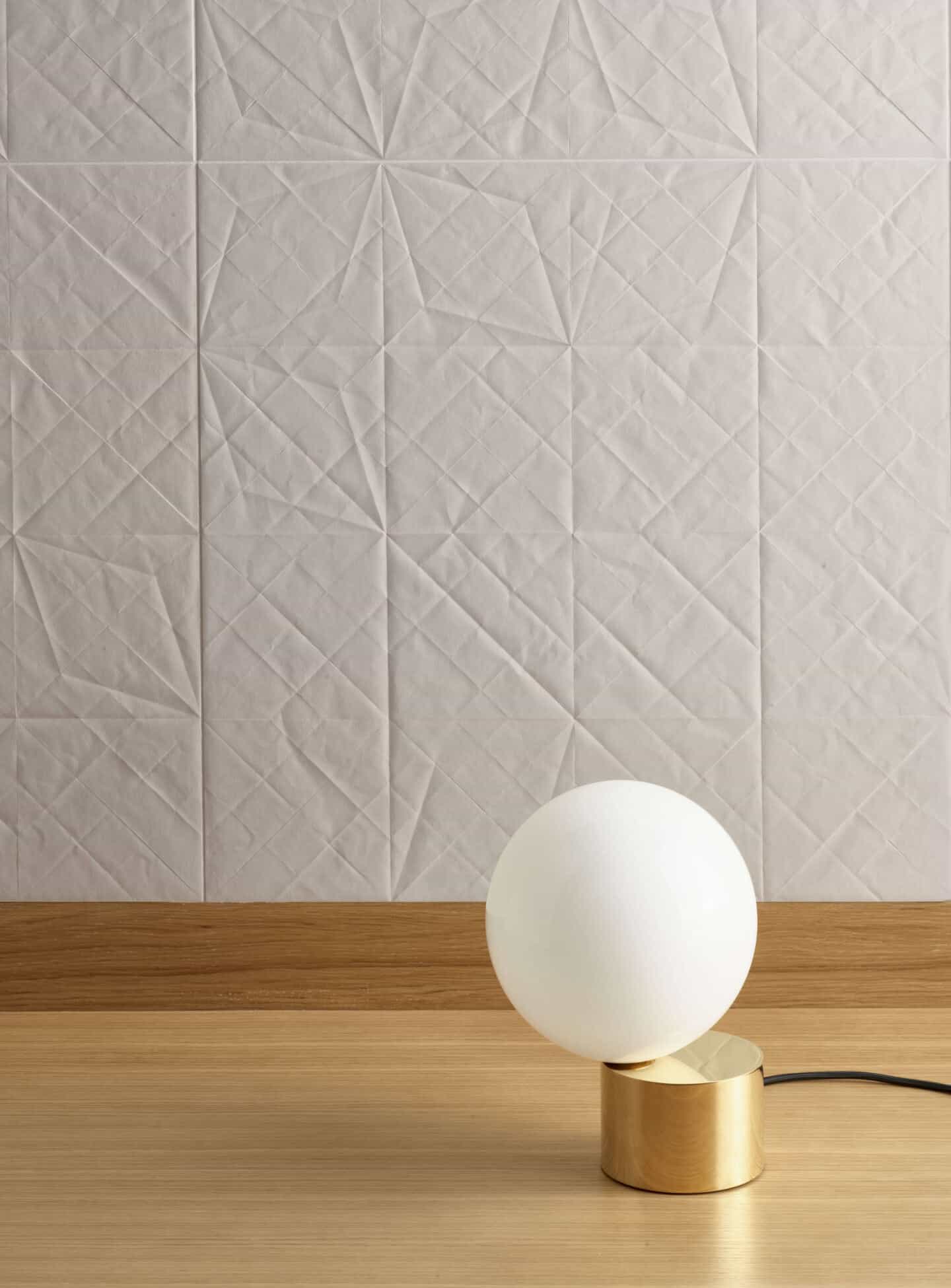 White textured wall tiles. A table light with a brass base is in the foreground.