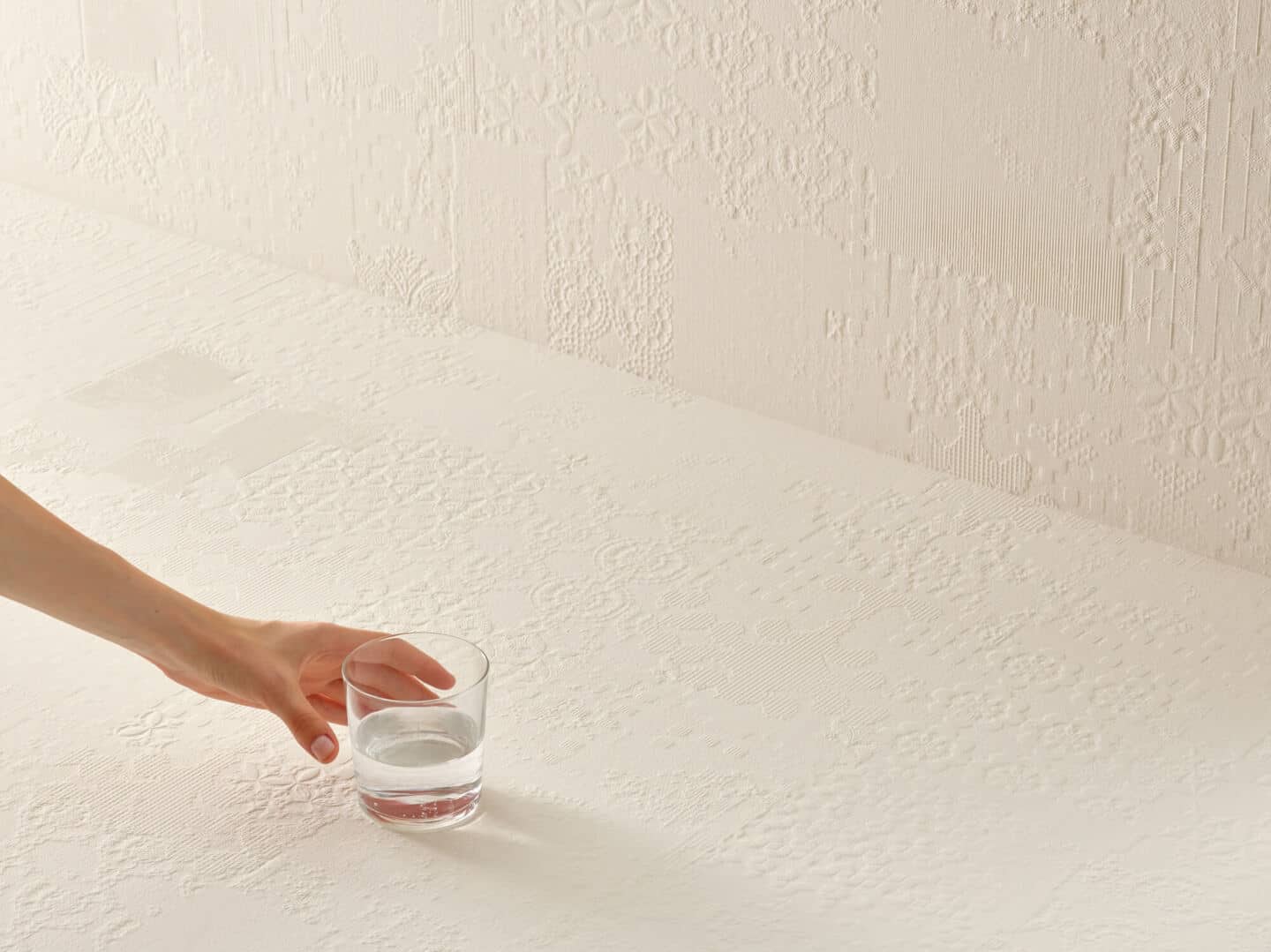 White textured wall and floor tiles. An arm is in the foreground reaching for a glass of water