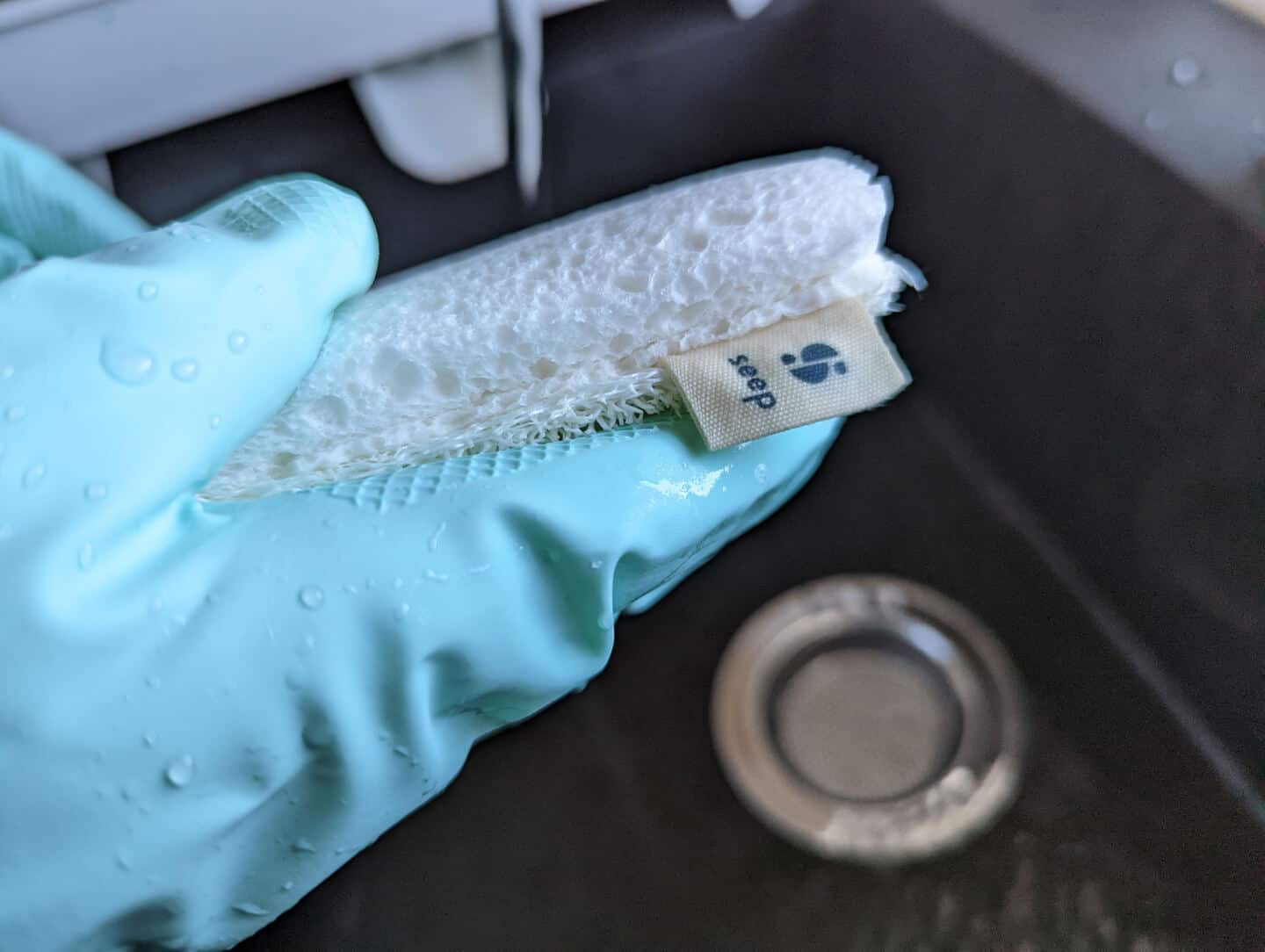 A close up of a plastic-free sponge scourer by Seep held in a hand wearing natural rubber gloves