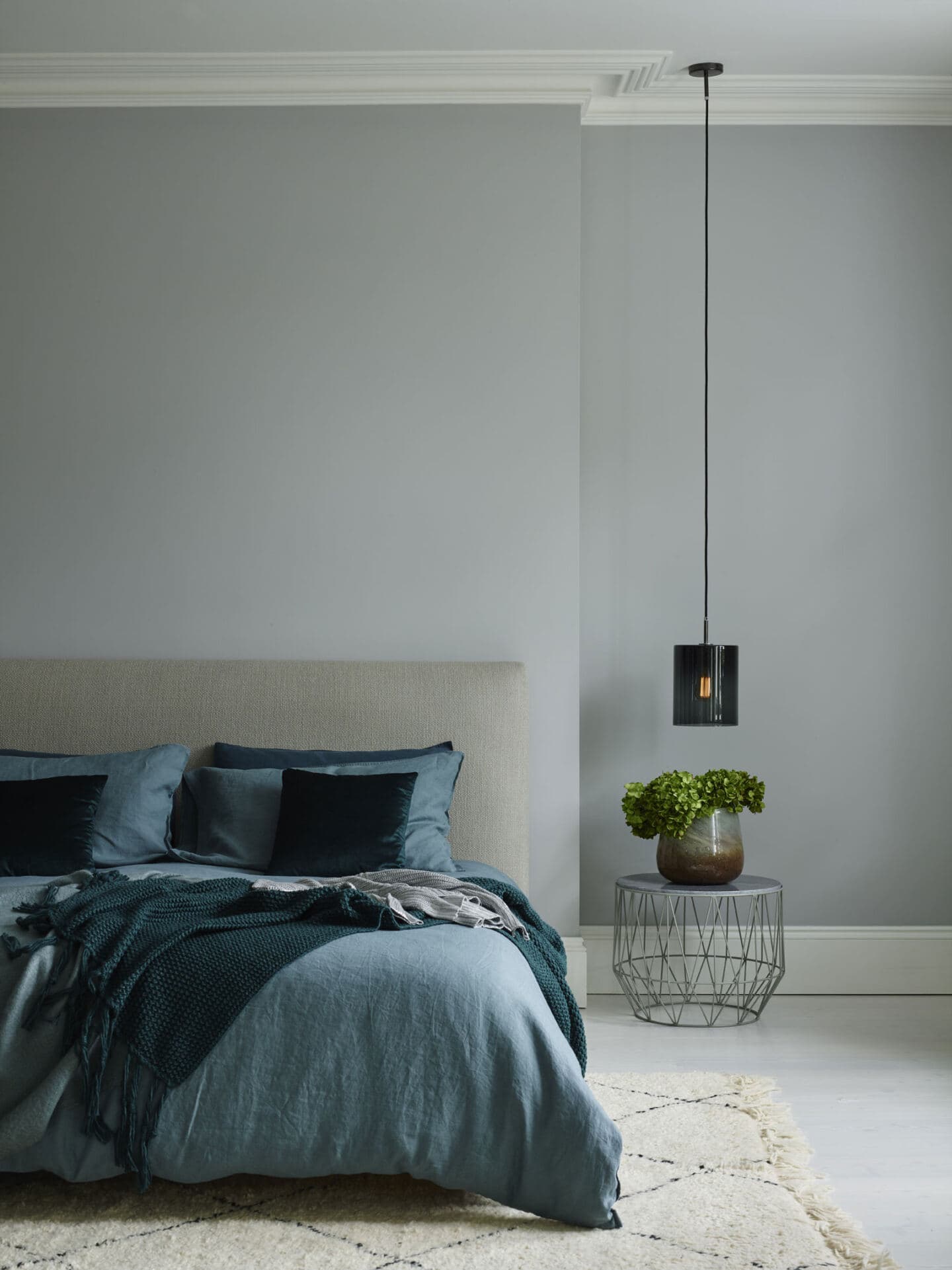 A pendant light hangs down beside a double bed covered in linen bedding in a blue bedroom