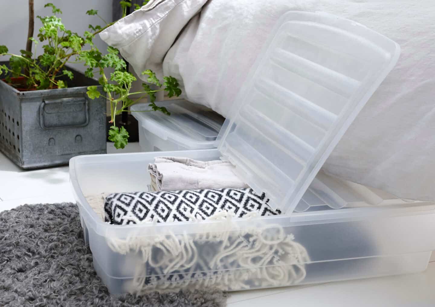 Blankets and clothing stored in a plastic box that rolls under the bed