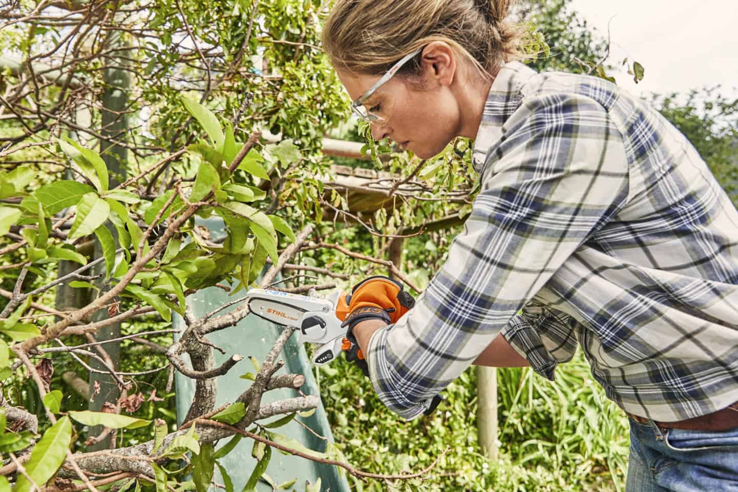 A woman trimming branches using a mini chainsaw