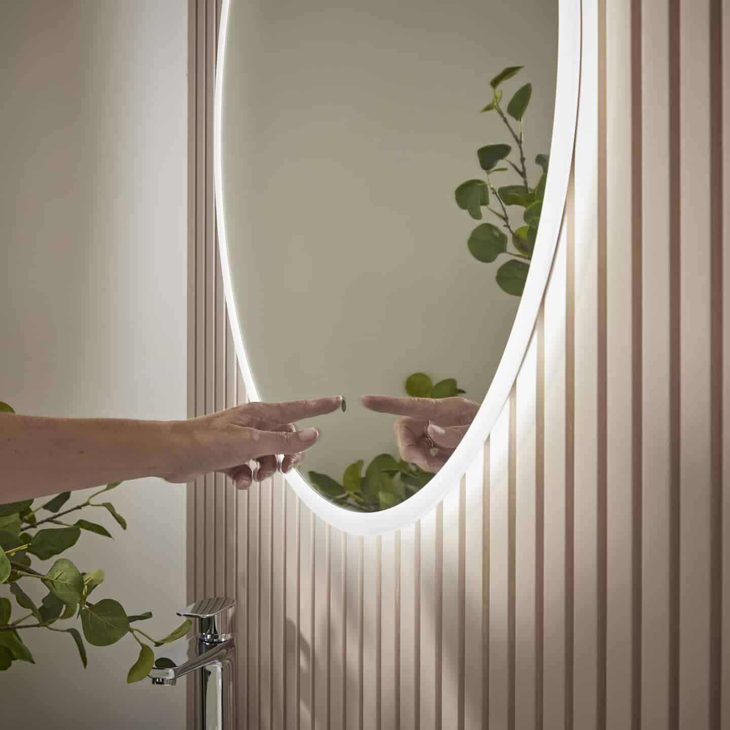 A hand switching on a sensor operated light on a circular bathroom mirror