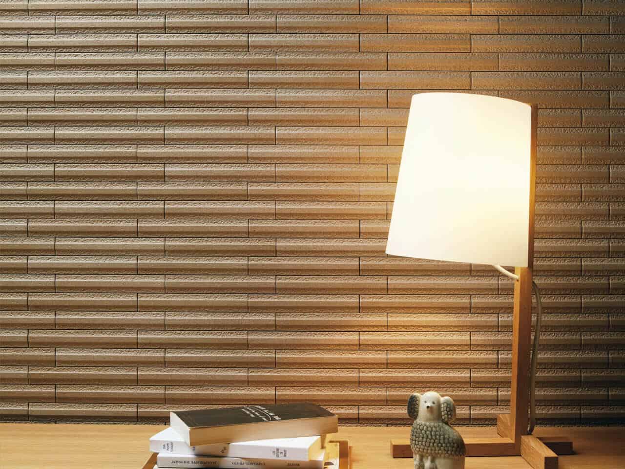 Granas textured wall tiles from Raven with a small table lamp and pile of books in front of the wall