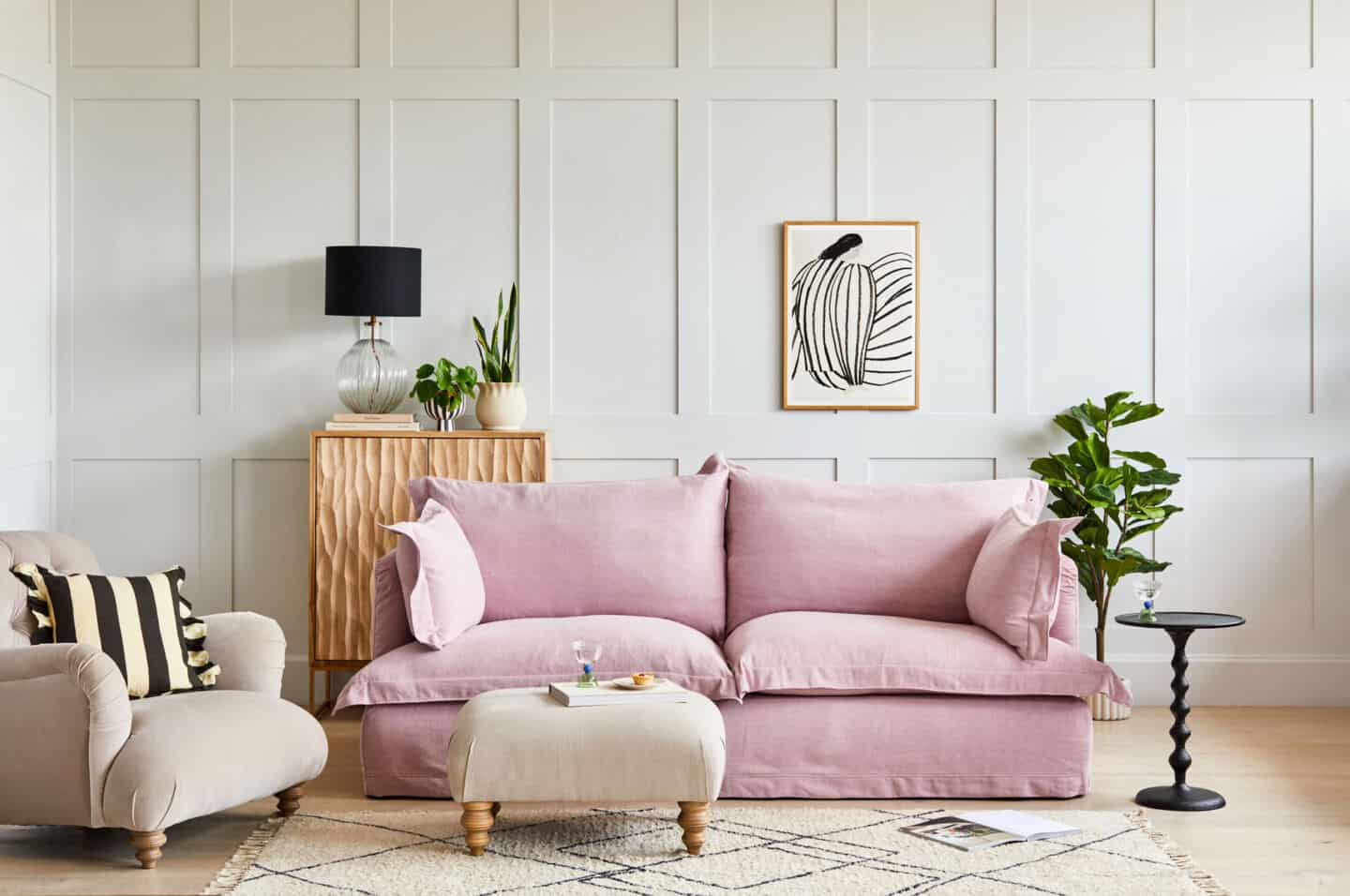 A pink sofa with removable covers set against a grey panelled wall with a berber style rug in front