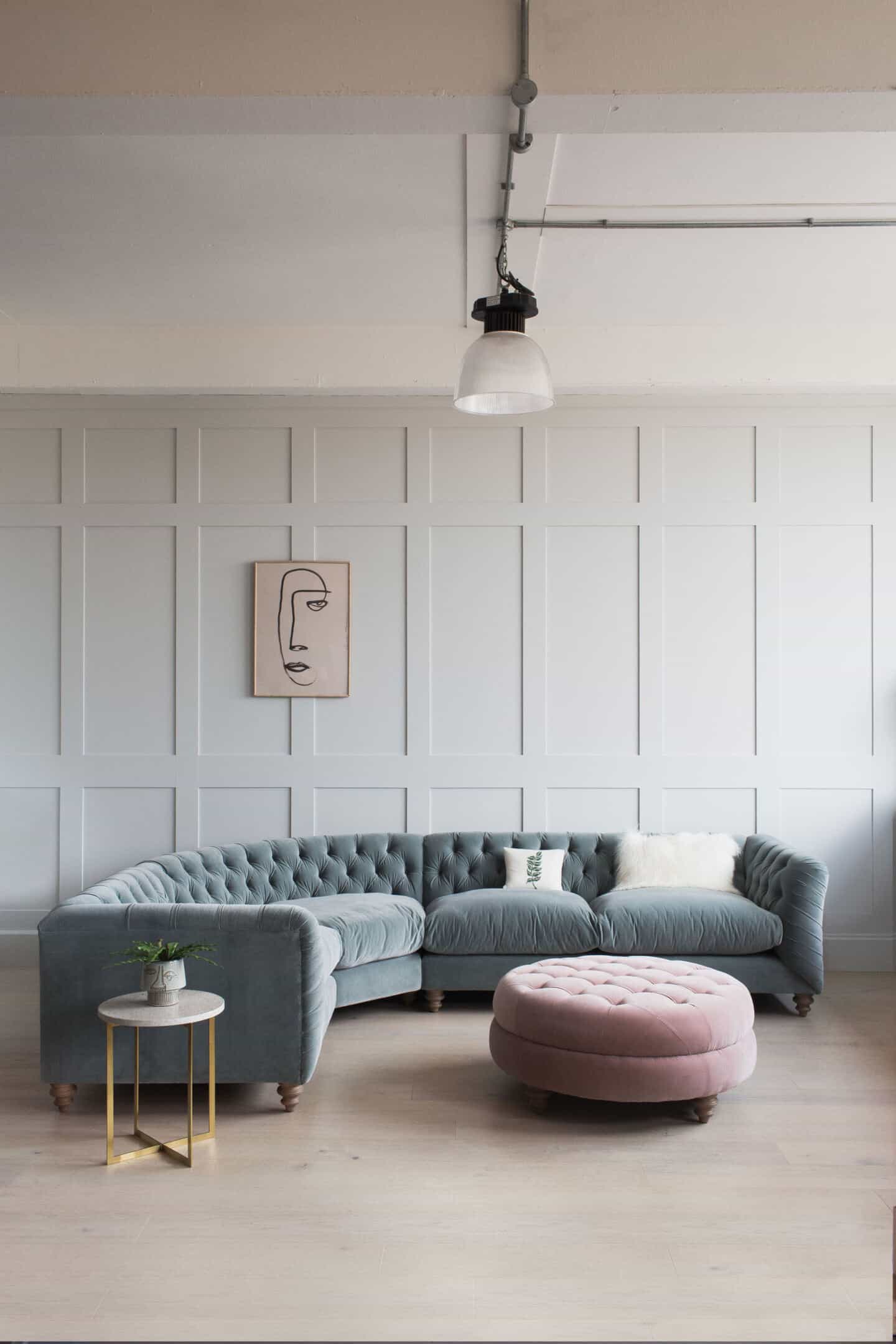 A curved Chesterfield sofa in blue velvet with a pink chesterfield style pouffe in front