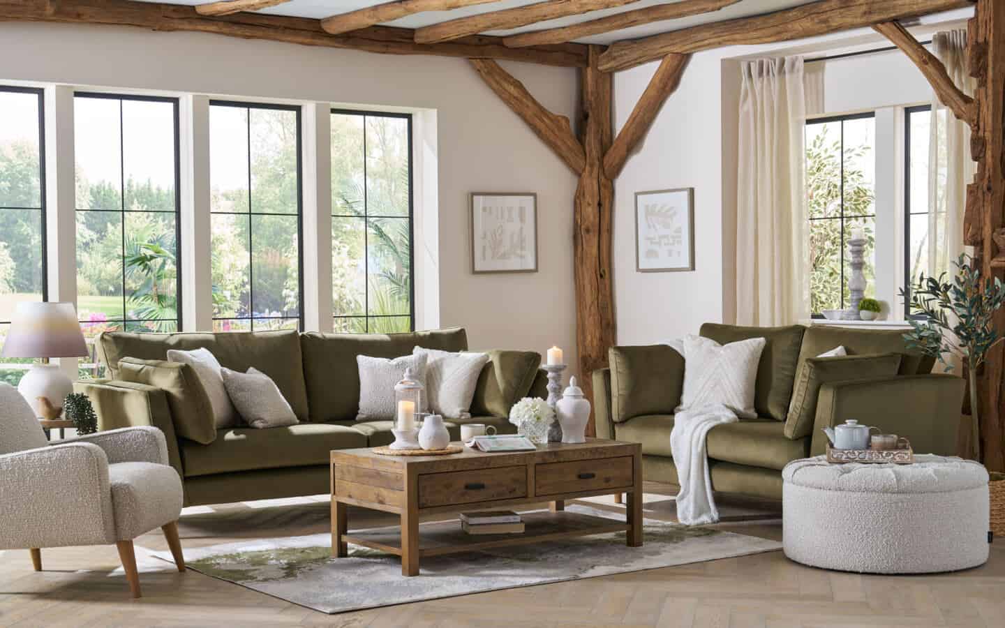 A minimal living room featuring wooden beams, large windows, green velvet sofas and a white boucle chair.