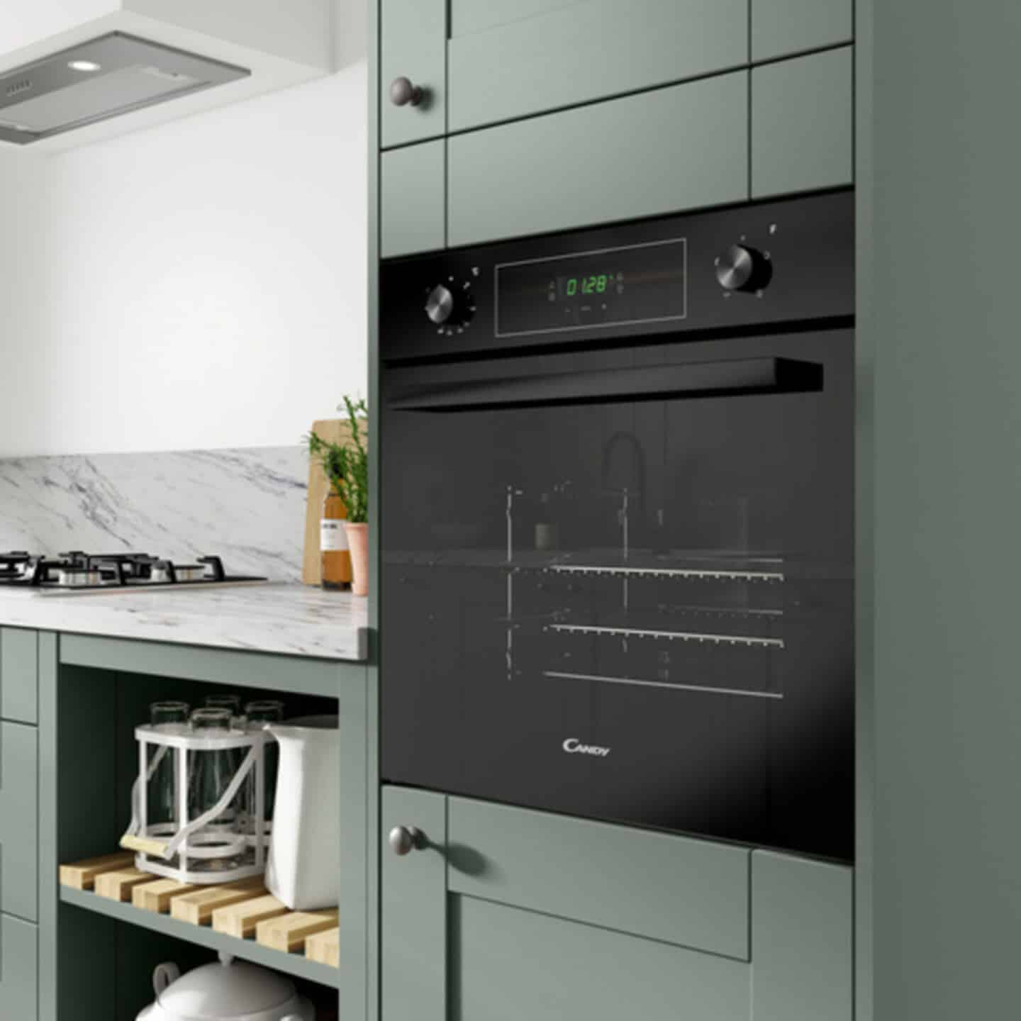 Close up of a built-in oven at waist height in a sage green kitchen with marble worktops