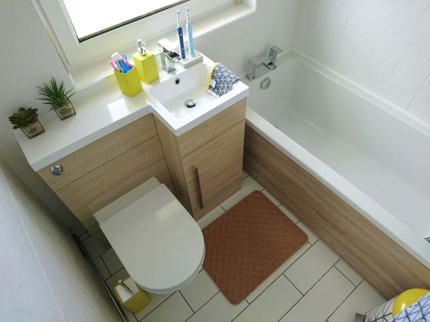 A super small bathroom with combined toilet and sink unit next to a bath. The wall and floor tiles are white.