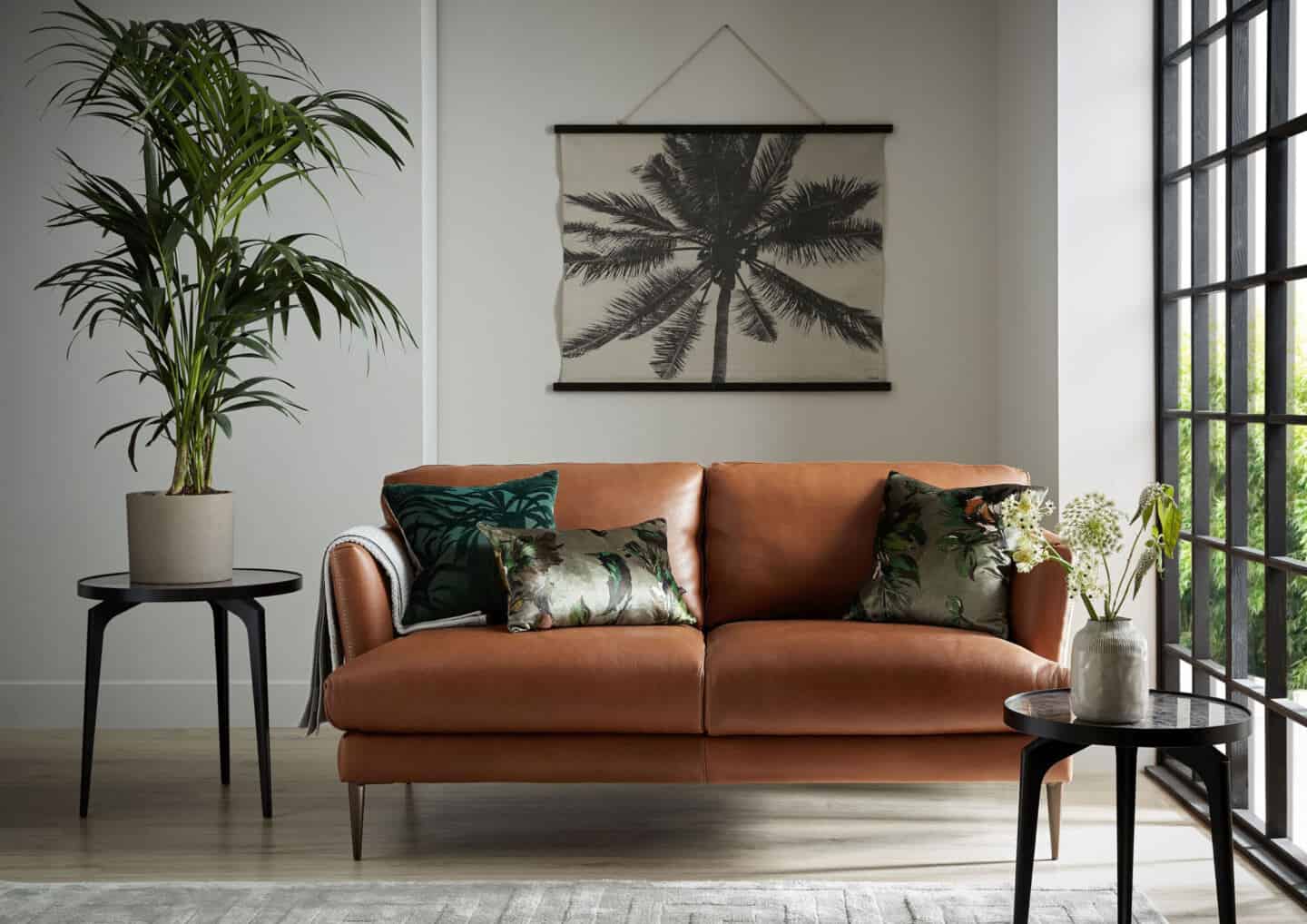  Bringing Natural Elements into the Home. Living room and  featuring a brown leather sofa with botanical cushions. A botanical wall hanging is on the wall behind and views through the window.