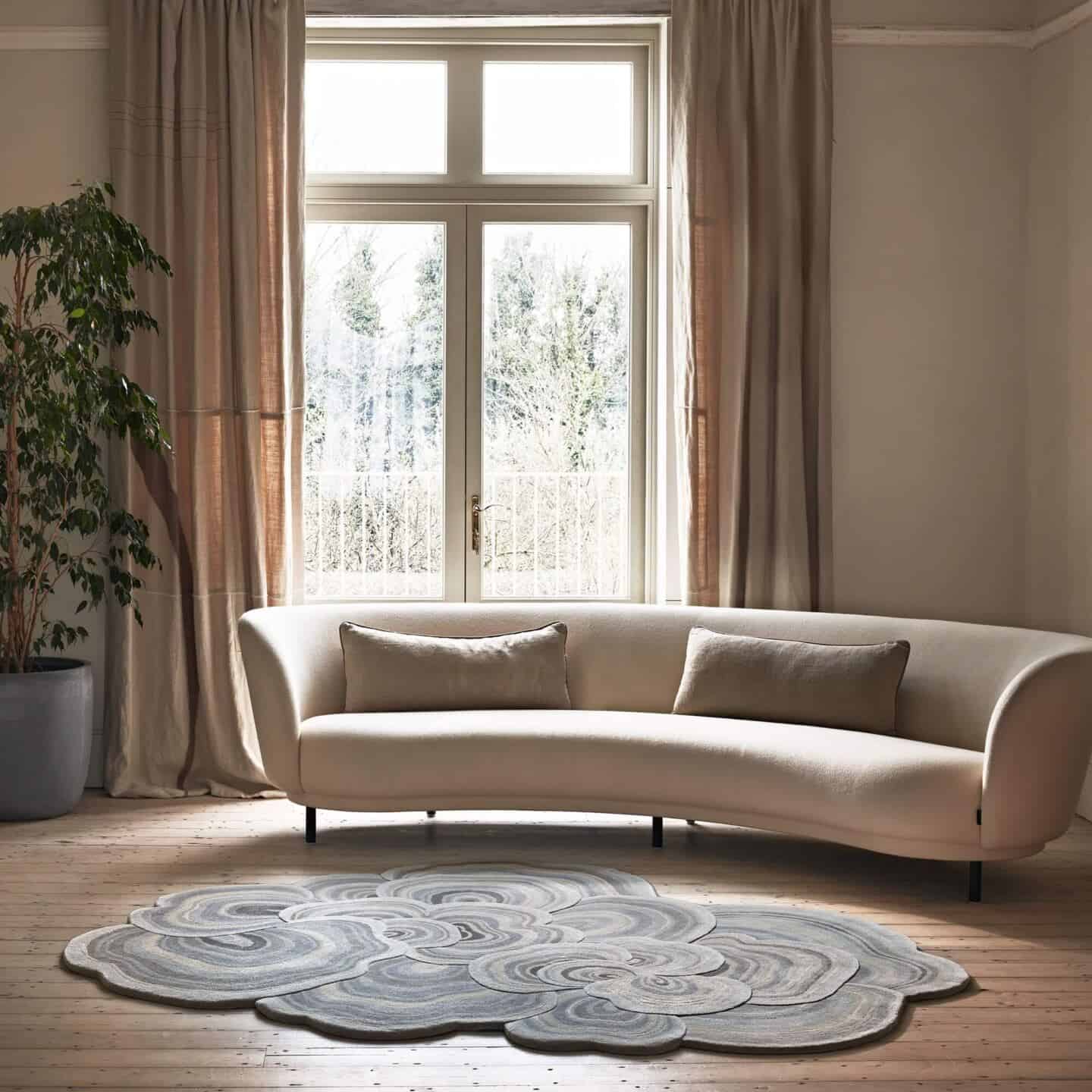 A curved cream sofa in front of French doors. An organic shaped rug on the floor in front