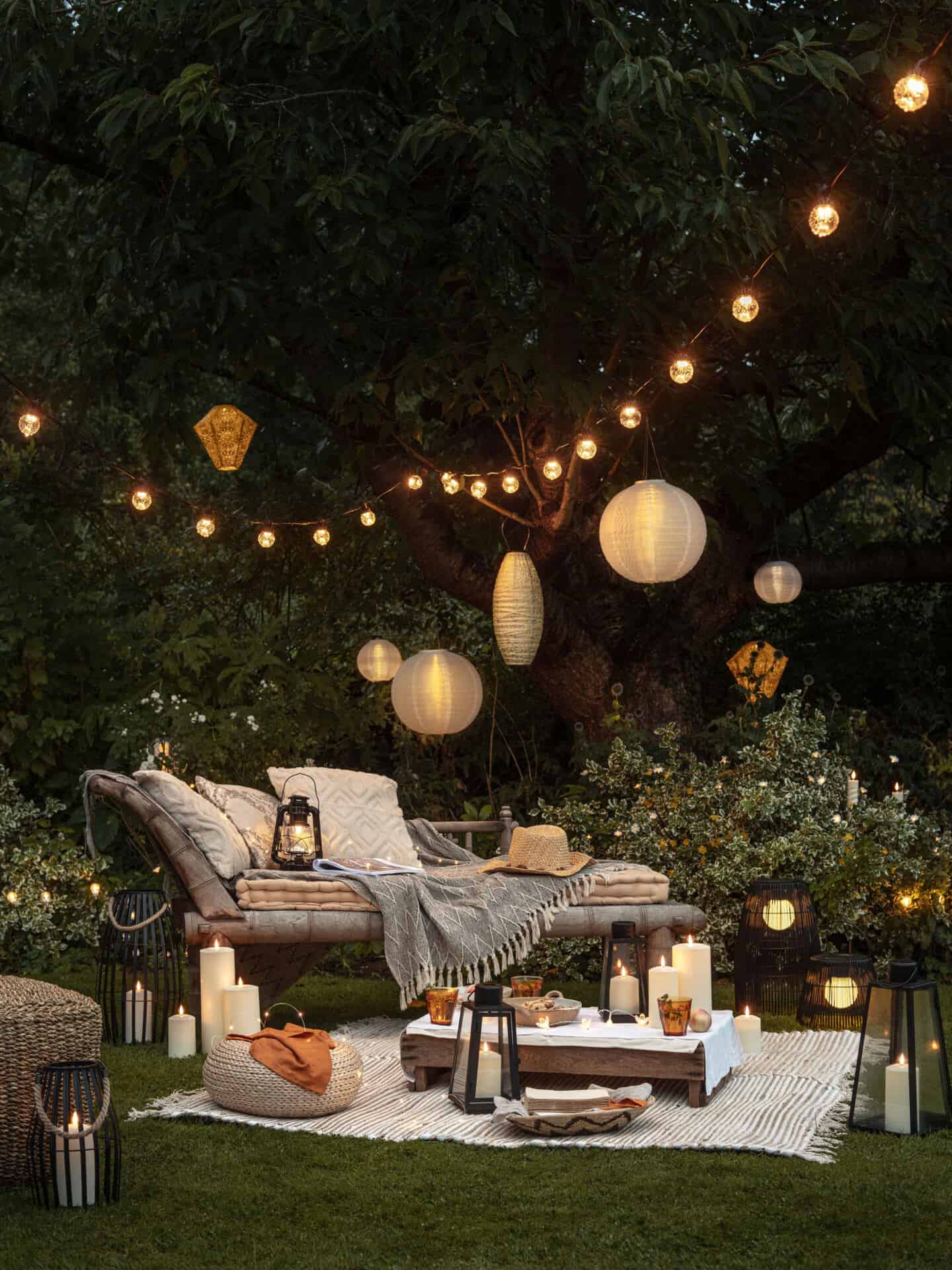 A garden bench with a blanket beside and a low wooden table surrounded by lanterns and LED candles