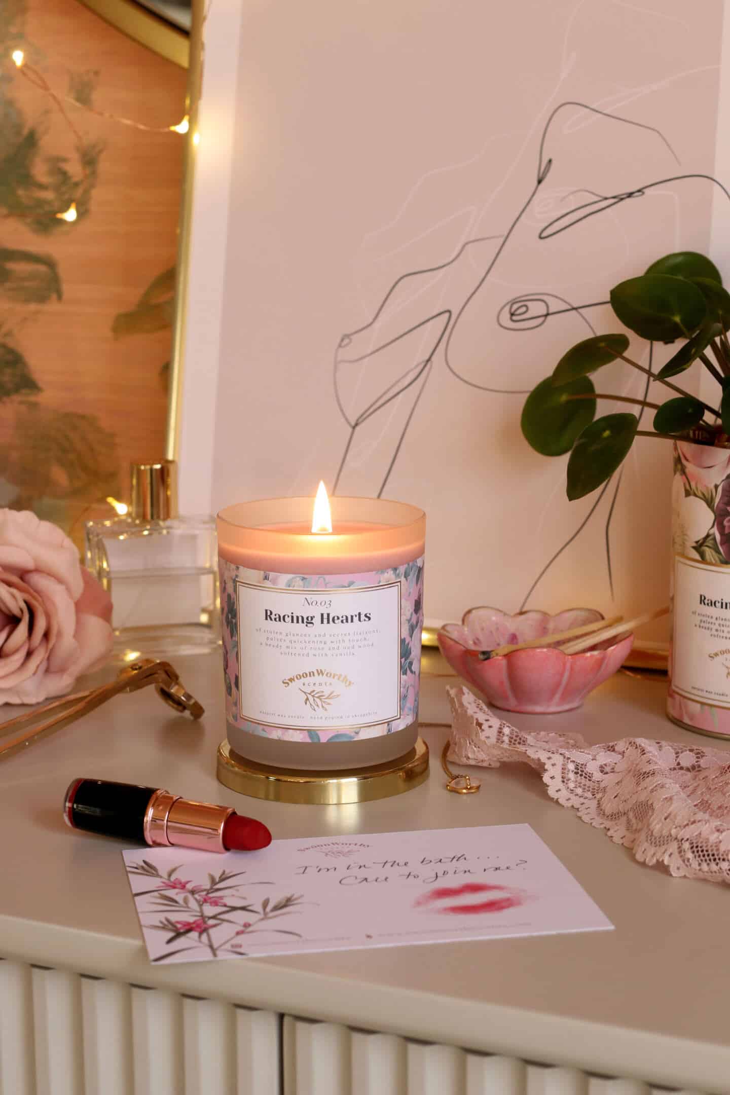 Racing Hearts, luxury eco-conscious scented candles by Swoon Worthy Scents on a chest of drawers in front of artwork and a bottle of perfume.