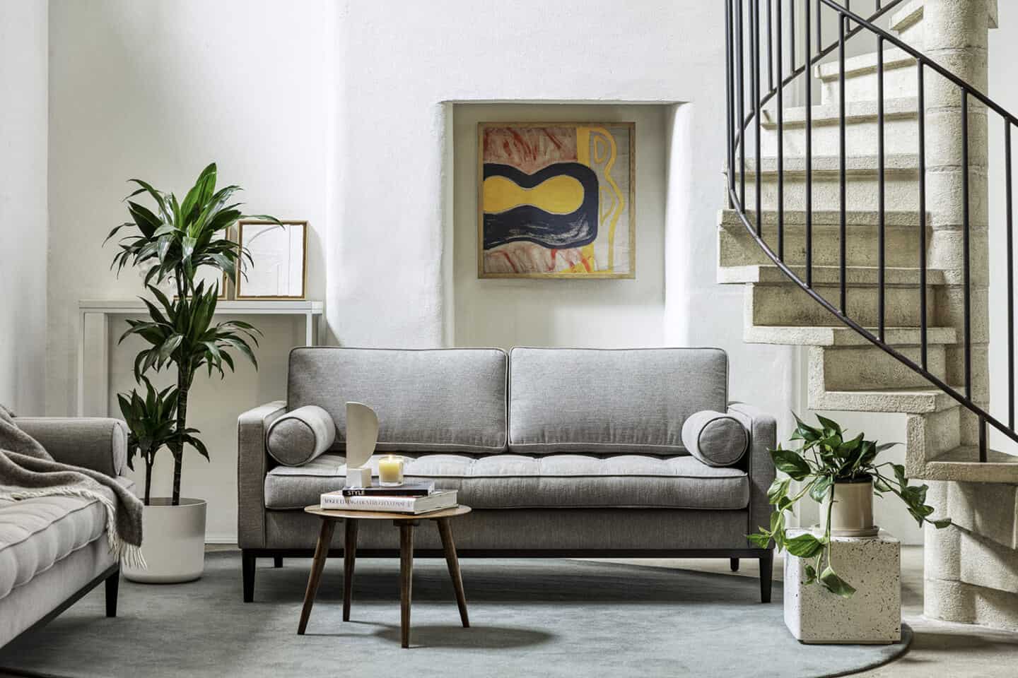 A grey sofa from Swyft Home on a round blue rug positioned next to a staircase