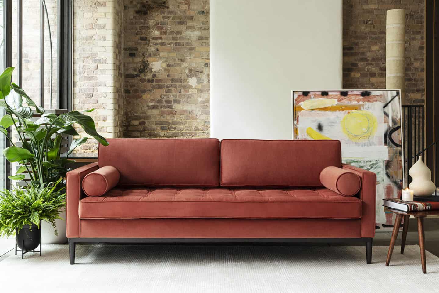 A blue sofa from Swyft Home on a grey rug, positioned next to a window and in front of a brick wall