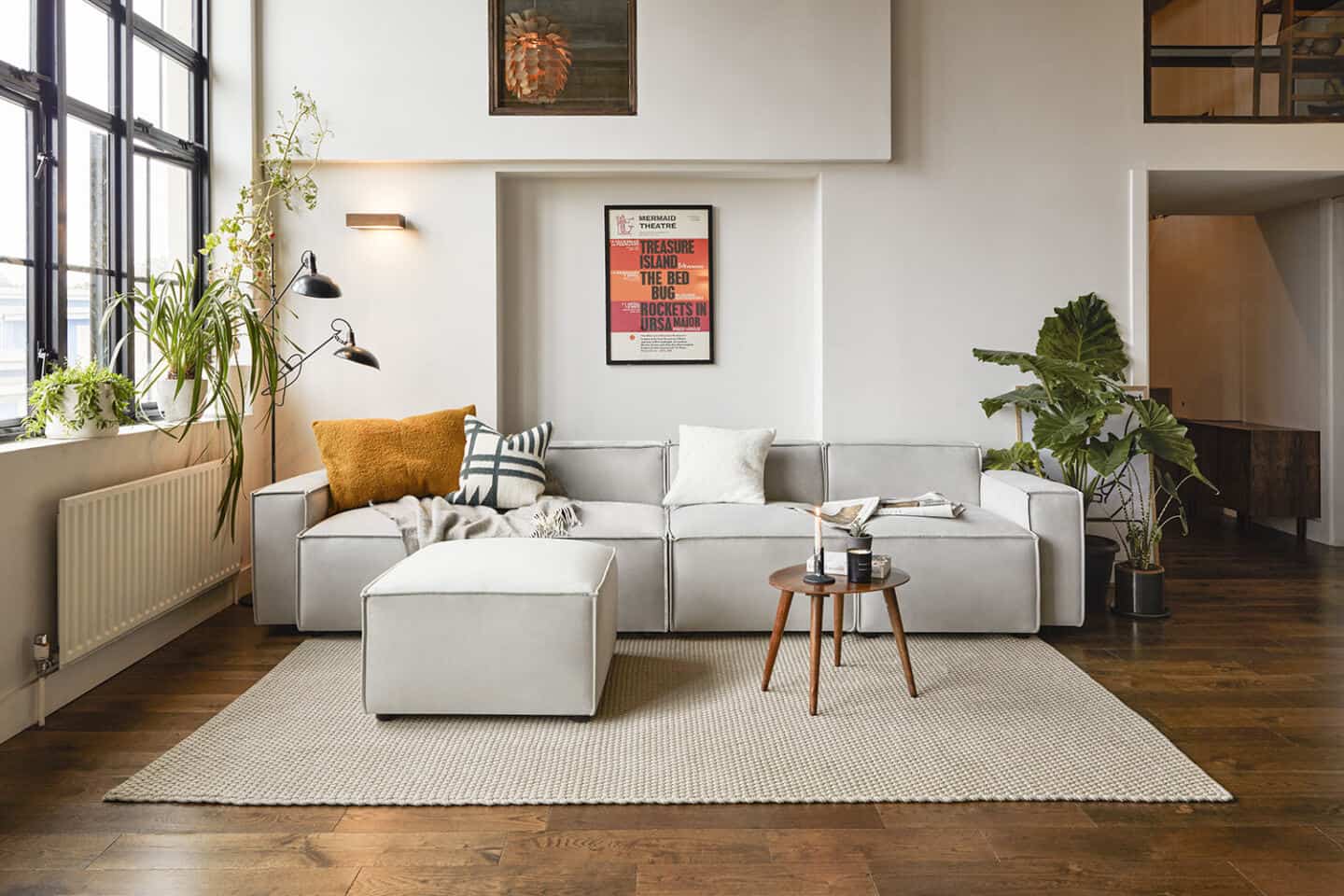 A grey sofa from Swyft Home on an oatmeal coloured rug, positioned next to a window and flanked by plants