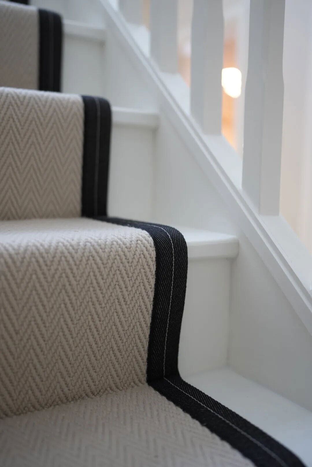 Grey carpet runner with black edging runs up a white staircase to create a dramatic statement