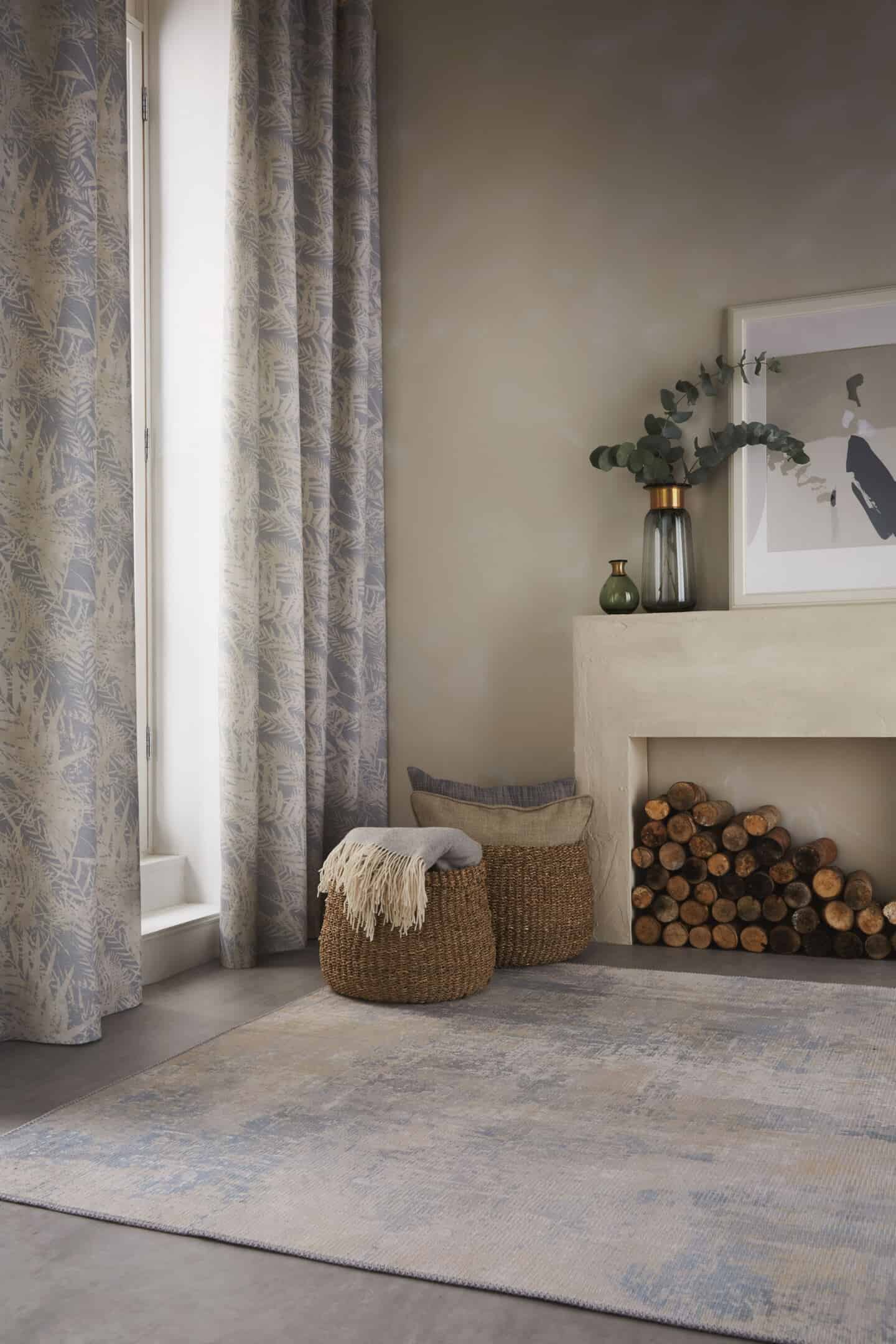 Textured Lives. Using texture in interiors to bring your home to life.  Curtains with a nature-inspired pattern on them hang in a doorway. Two baskets next to a fireplace full of throws blankets and cushions. 