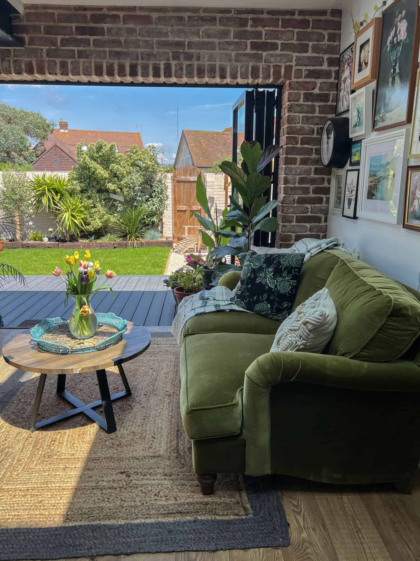 A living room containing a green velvet sofa that opens up onto the garden decking