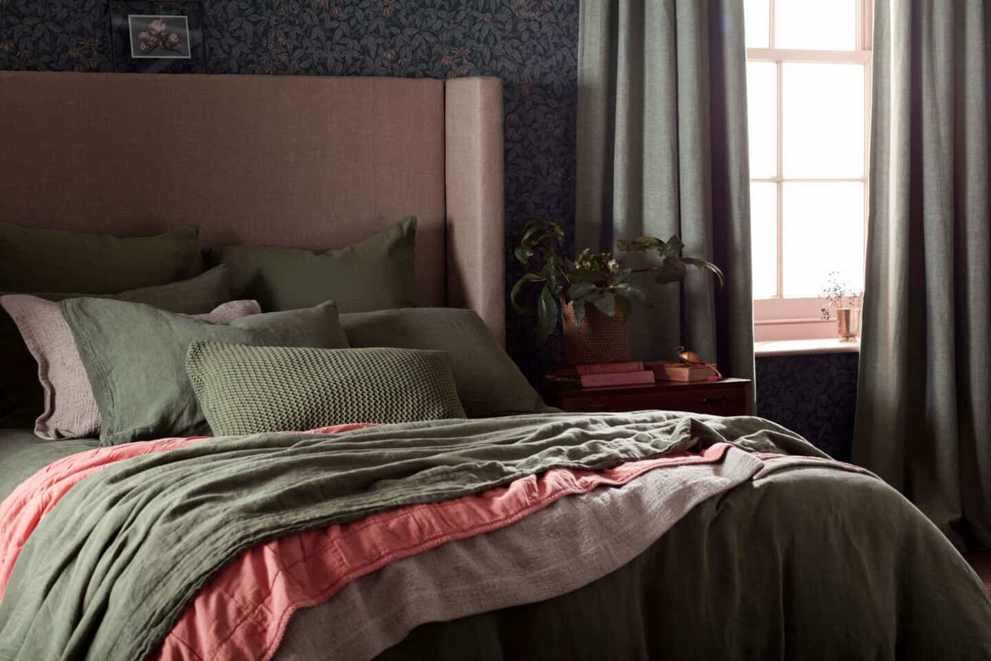 A cosy bedroom featuring a bed with large linen headboard and pink and green linen bedding