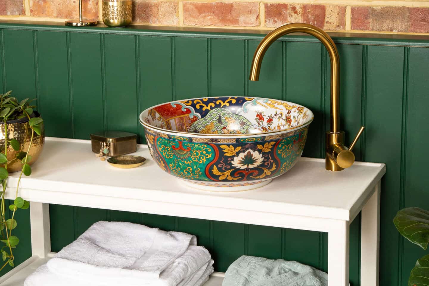 An round bathroom basin with oriental style pattern and colours rests on a vanity unity in front of a green wall