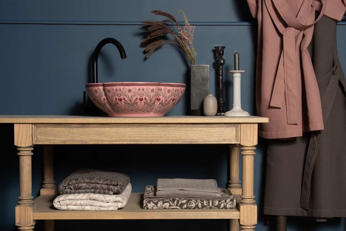 A scalloped pink bathroom basin with delicate floral patterning rests on a wooden vanity unit with a blue wall behind