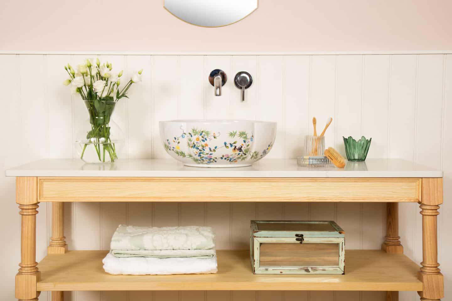 A round white bathroom basin with floral patterning rests on a wooden vanity unit