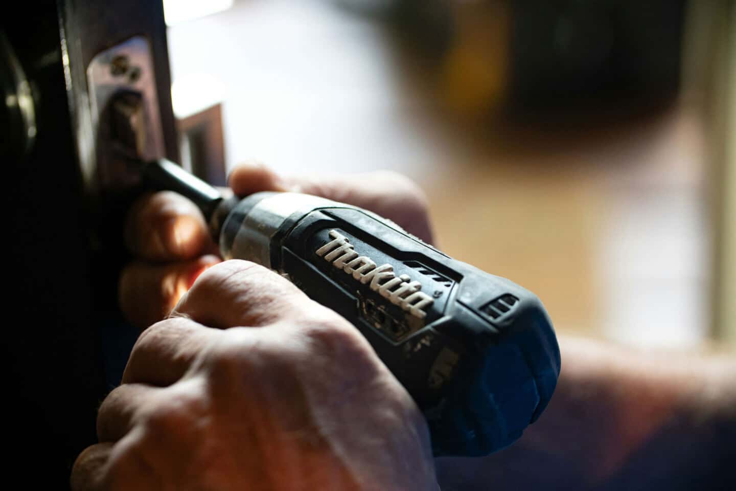 A man holding a Makita drill fixing the lock on a door