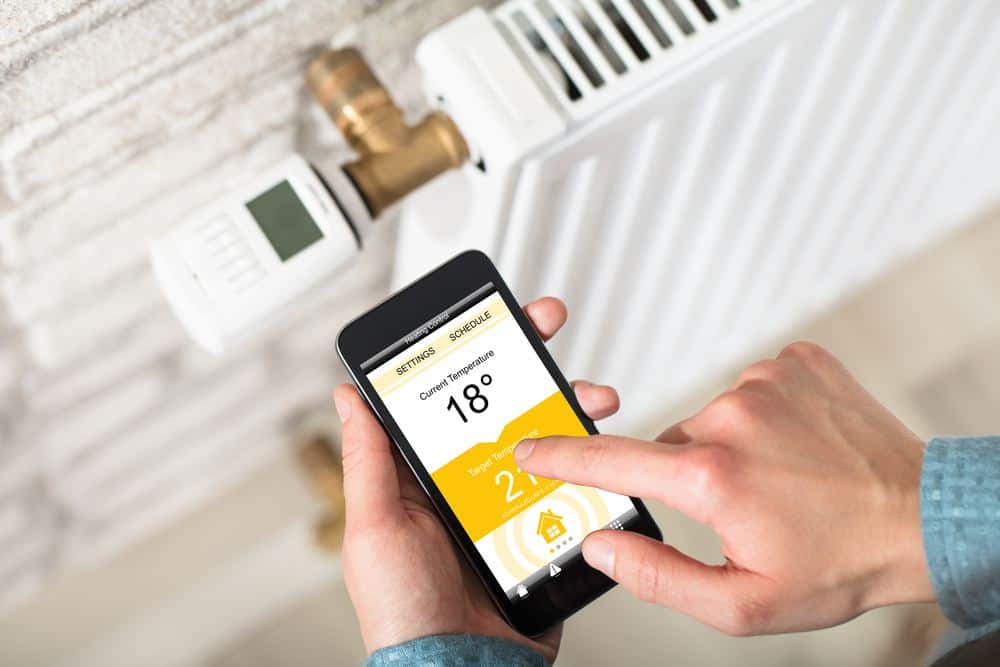 Man's hand operating a Thermostatic Radiator Valve on his smart phone