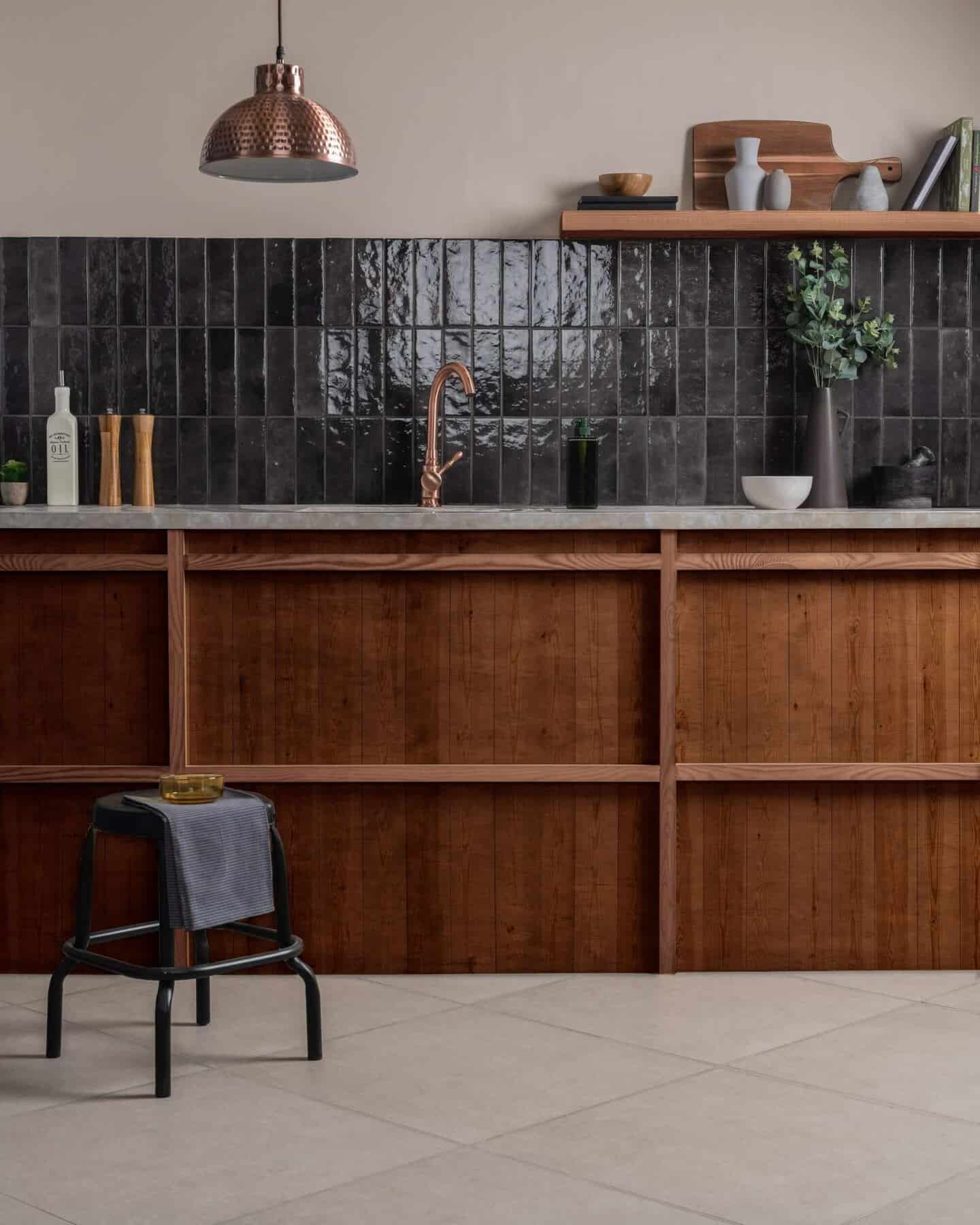 A wooden kitchen with stone floor tiles and vertical glazes tiles in green