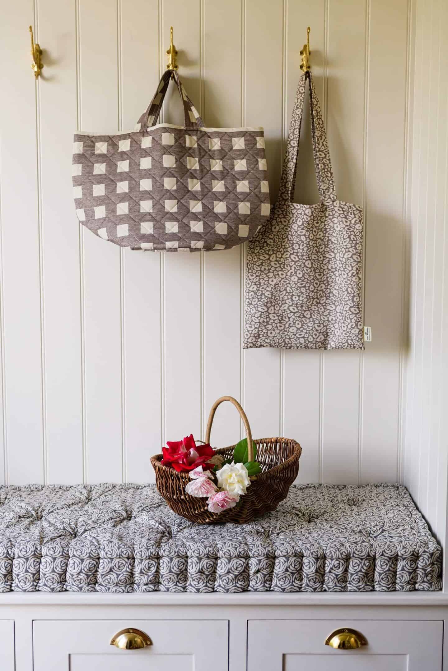 two reusable cotton shopping bags hang on hooks above a bench seat