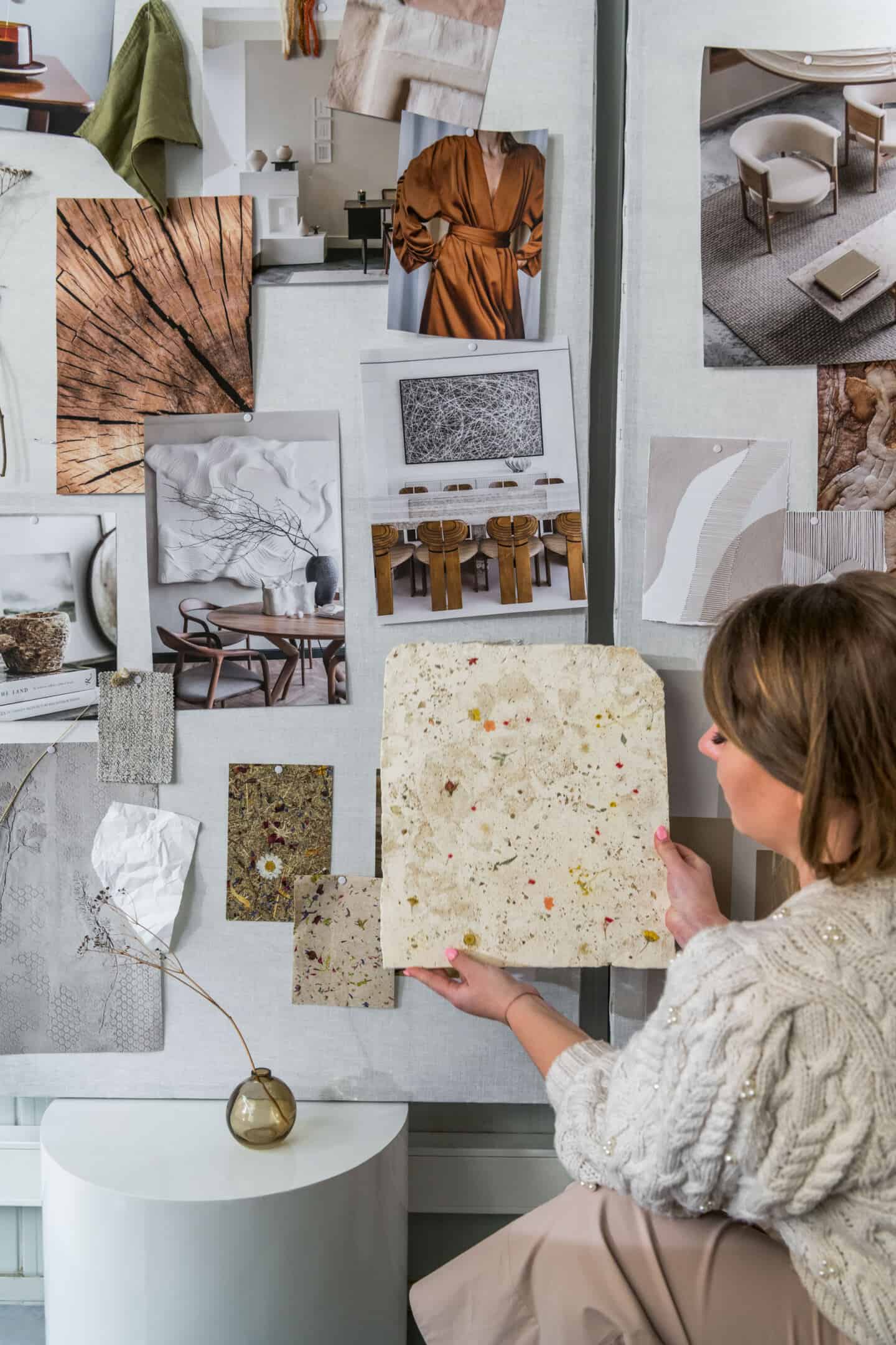 Anastasiia Kudashova, Chief Designer at Quick-Step holds up a slab of concrete with wild flowers embedded in it against a moodboard on the wall full of nature-inspired images and fabric swatches