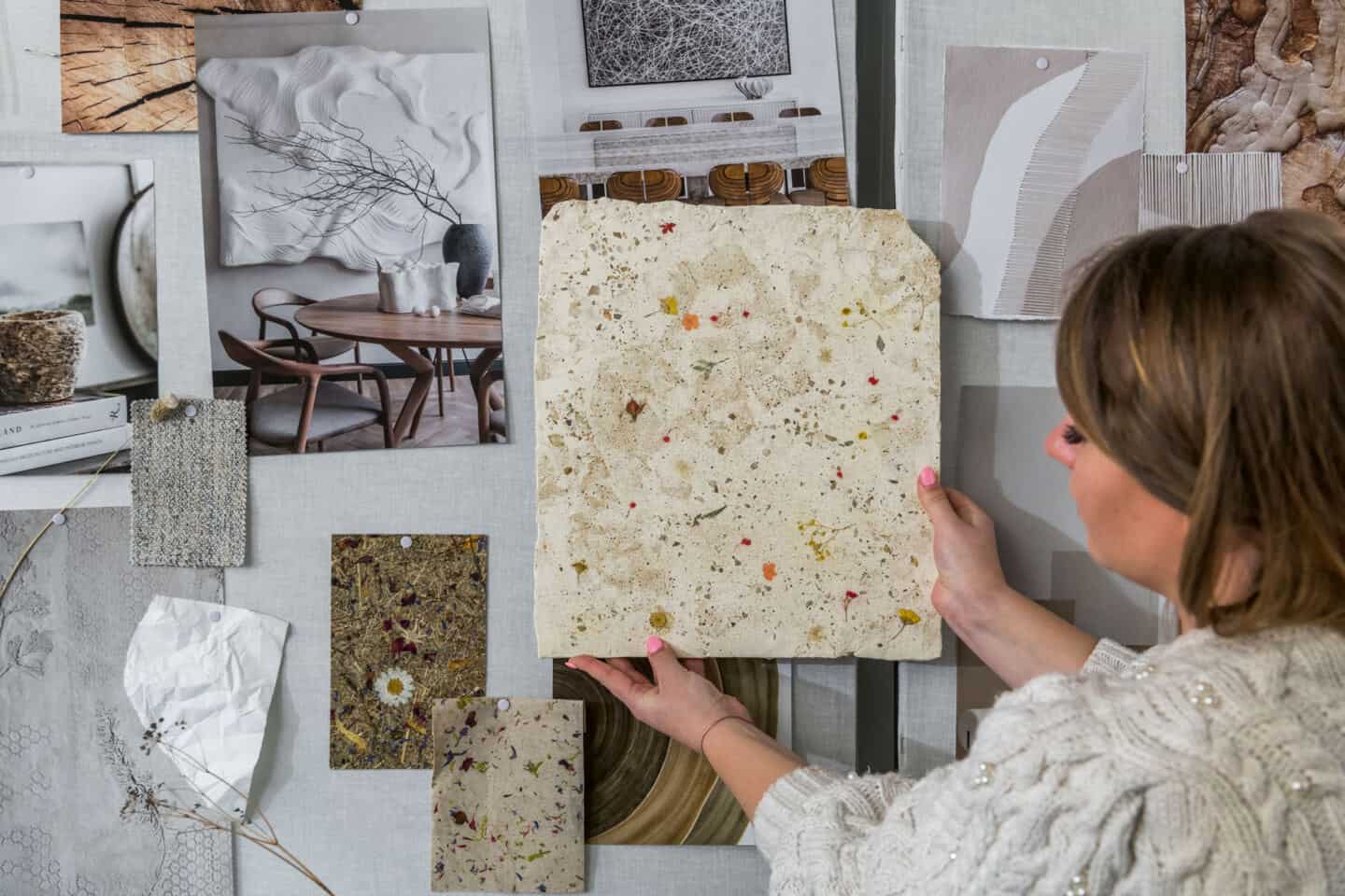 Anastasiia Kudashova, Chief Designer at Quick-Step holds up a slab of concrete with wild flowers embedded in it against a moodboard on the wall full of nature-inspired images and fabric swatches