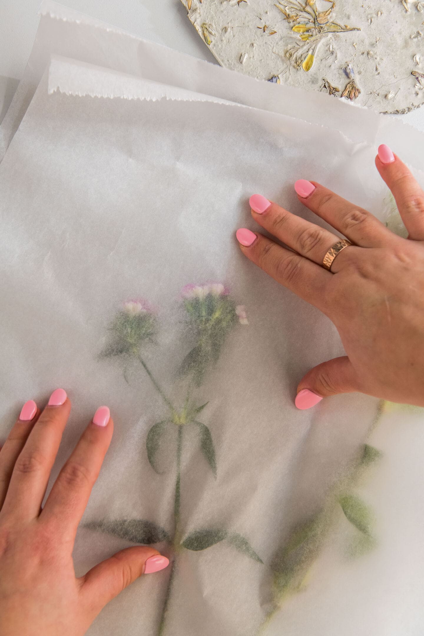 Anastasiia Kudashova, Chief Designer at Quick-Step places a flower stem between two pieces of grease proof paper. A slab of concrete with wildflowers embedded in it lays next to the paper.