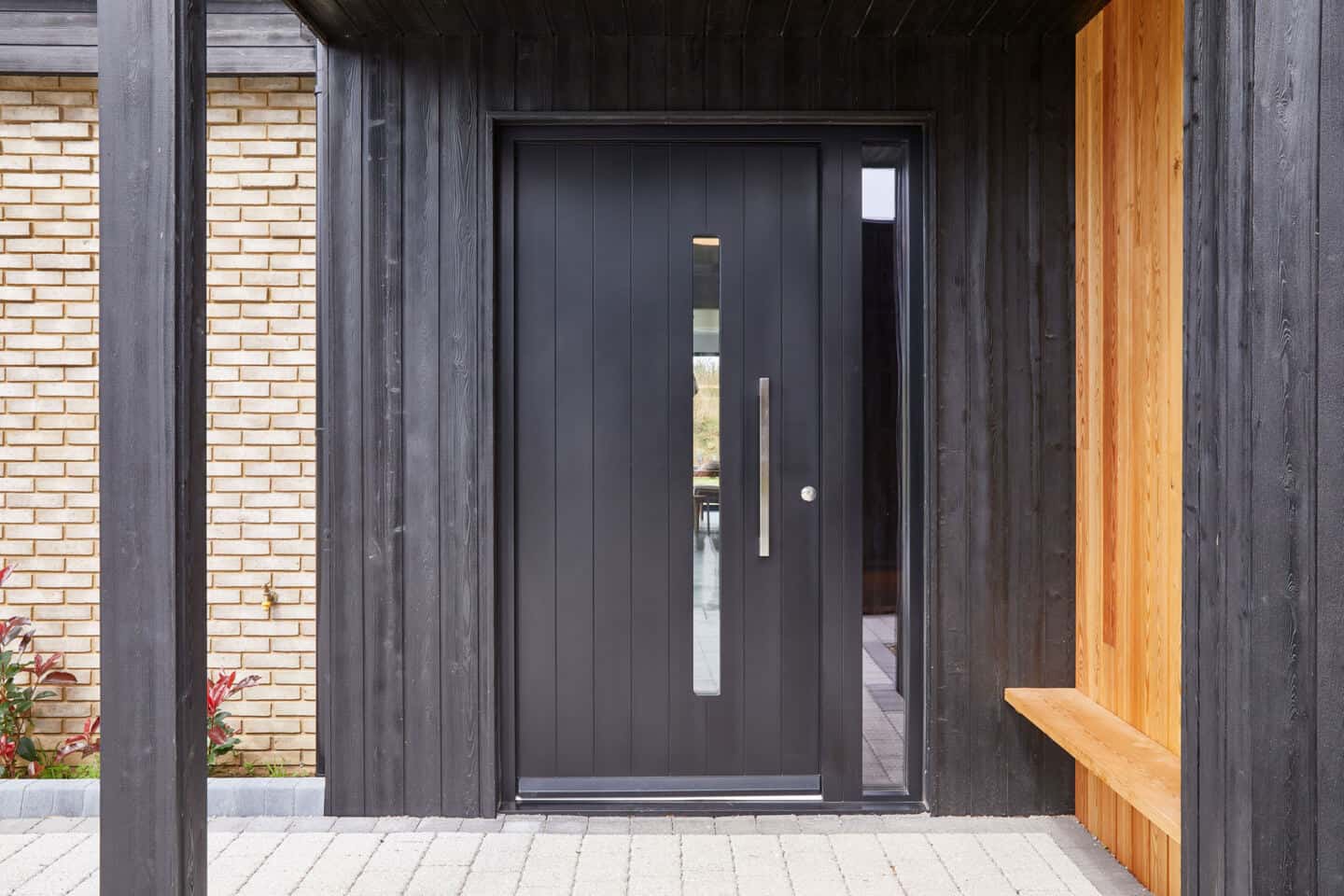 A black front door on a modern home made from brick and charred black timber. 