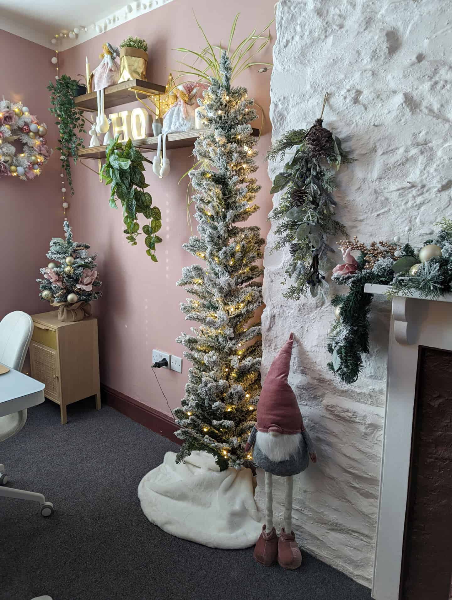 A gonk stands next to a flocked Christmas tree in a pink home office