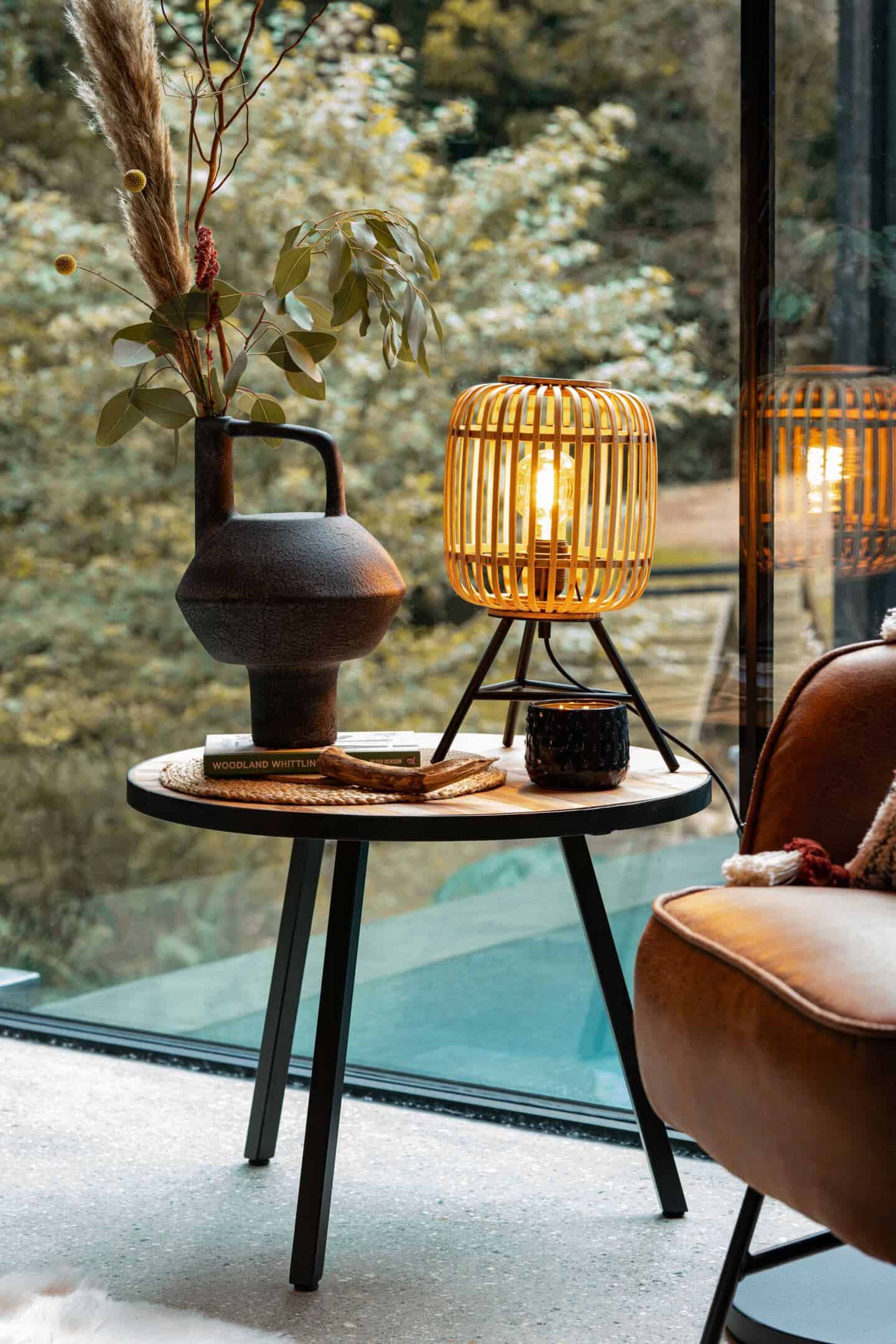 A table light and vase on a wooden side table from Wayfair in front a large glass window that overlooks a small infinity pool at the Wildwood Spa in North Devon