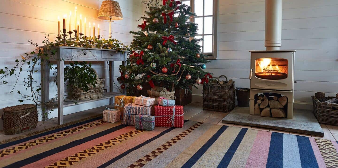 A wood burner next to a Christmas tree with presents on a Weaver Green recycled plastic rug in a sustainable home