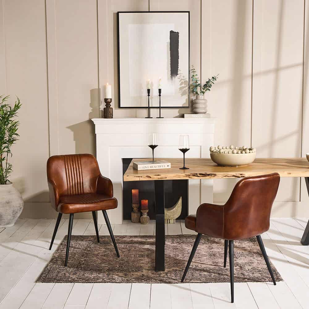 a neutral dining room with wood panelled walls, a faux fireplace, leather chairs and a wooden dining table with rug beneath