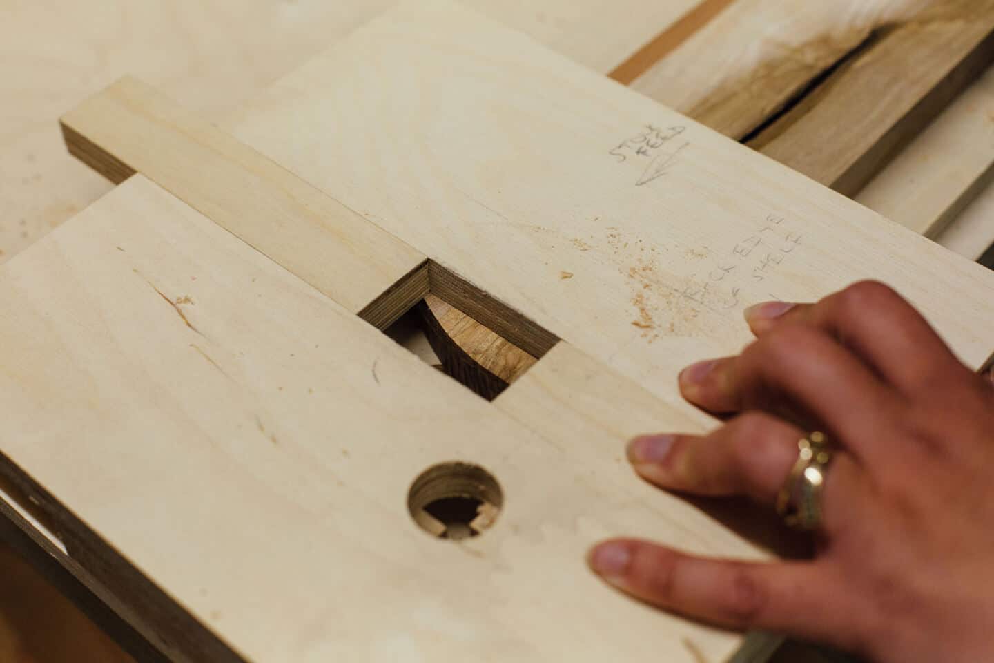 A woman's hand holds a jig in place before routing a piece of wood 