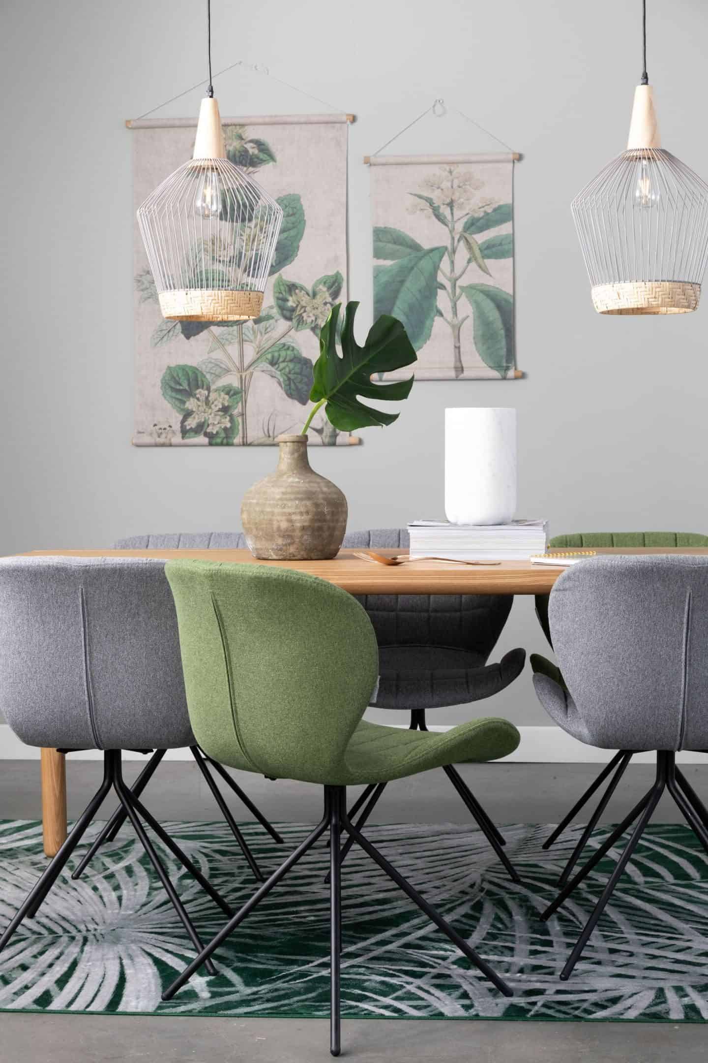 A desk or dining table with chairs around and two pendant lights suspended above. Botanical prints hang on the wall behind. 